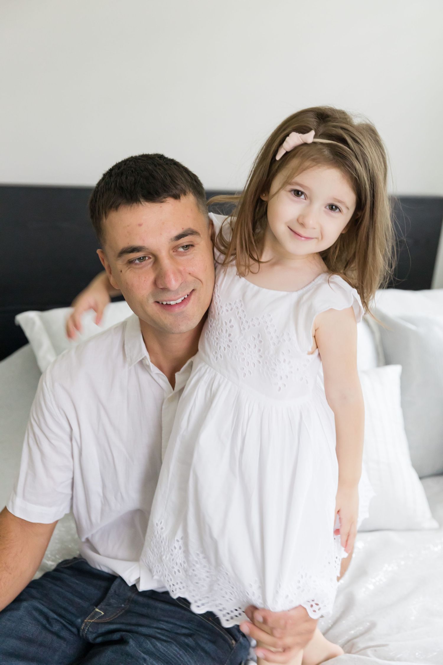 Family portrait on bed showing parent and child in matching white outfits.