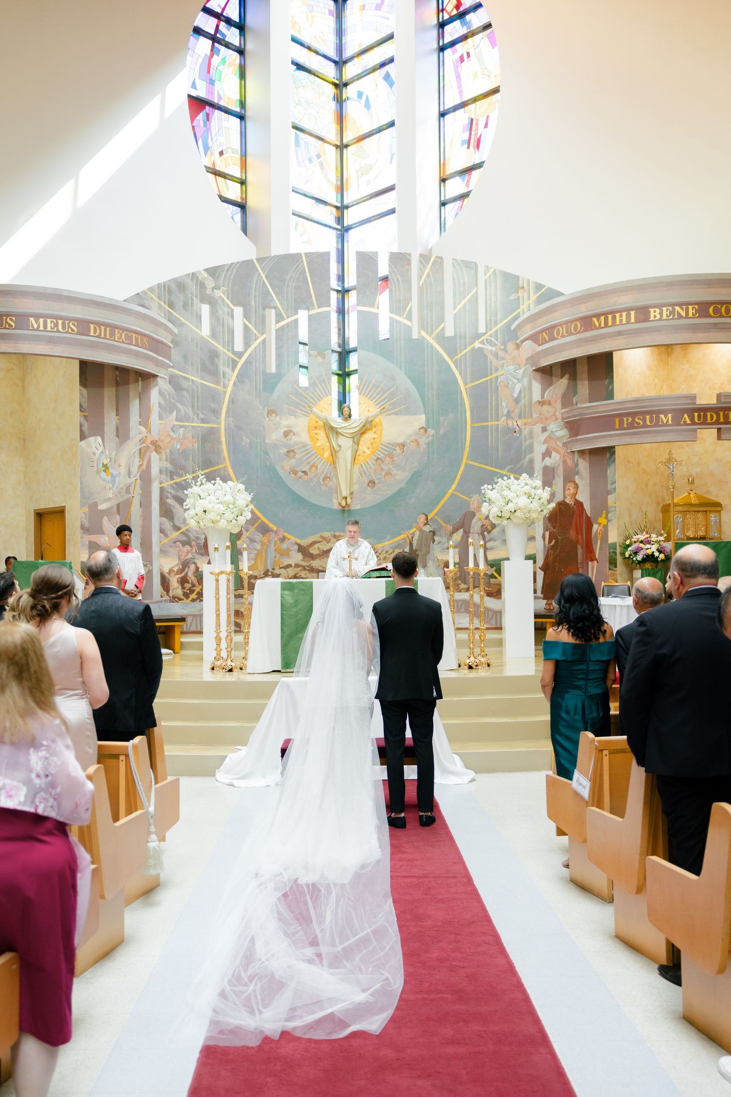 Wedding ceremony in a church with stained glass windows and decorative altar in the background.