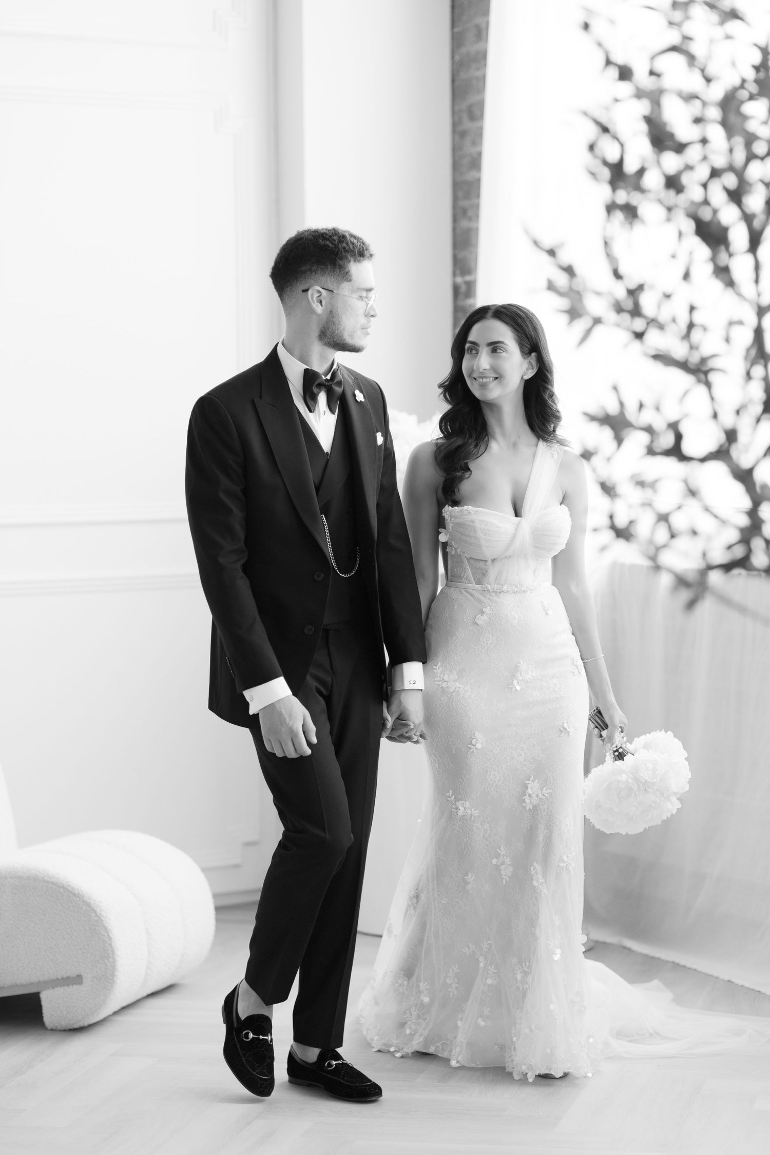 Black and white portrait of newlyweds standing together in an elegant bright interior setting.