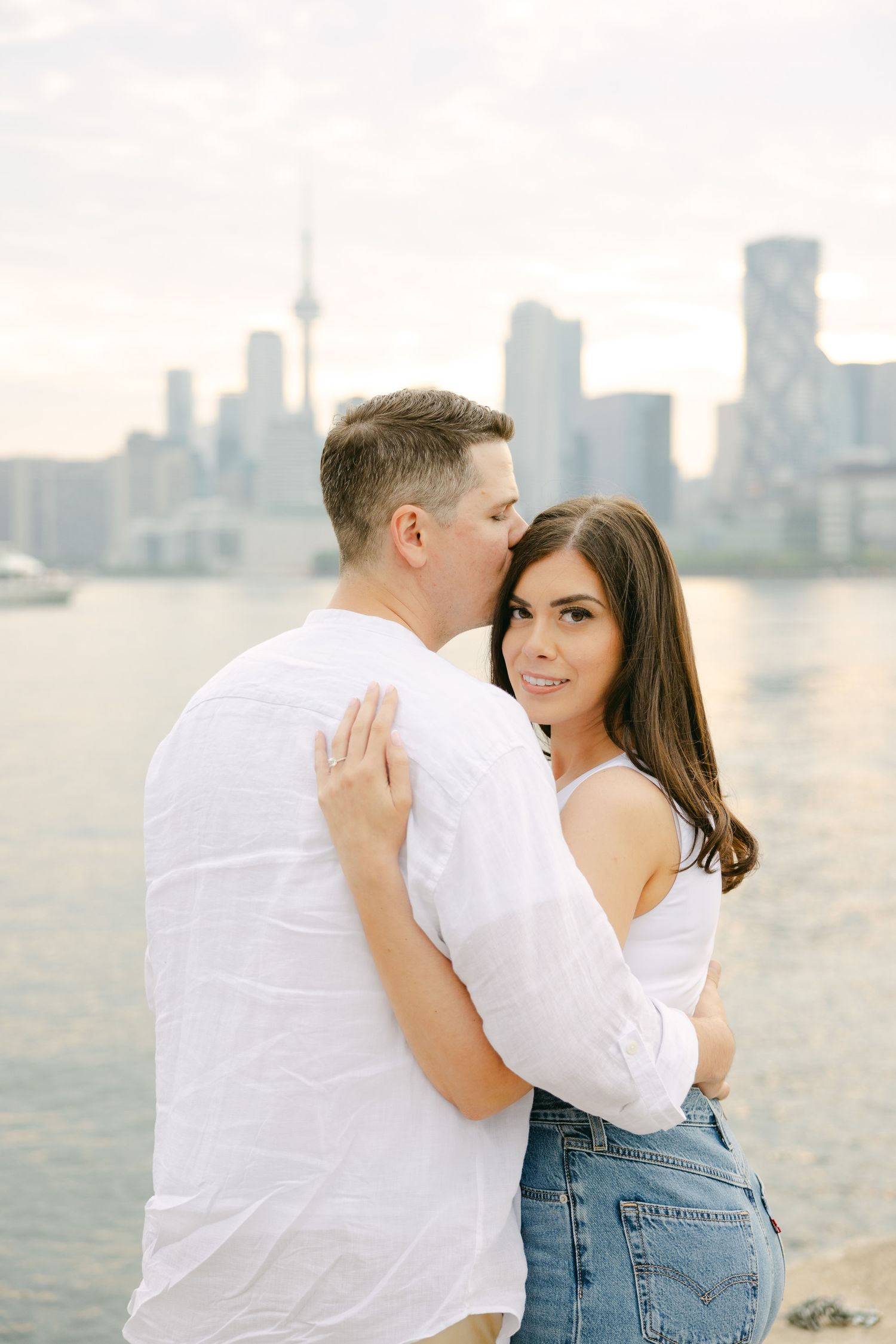 A couple shares an intimate moment near the waterfront with Toronto's distinctive skyline behind them.