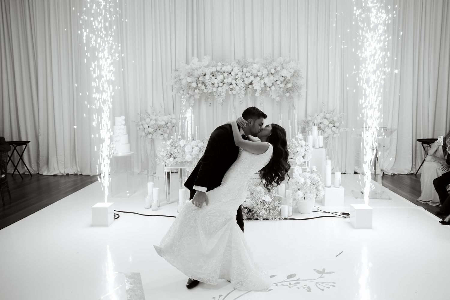Dramatic black and white wedding photo with sparklers and white floral arrangements.