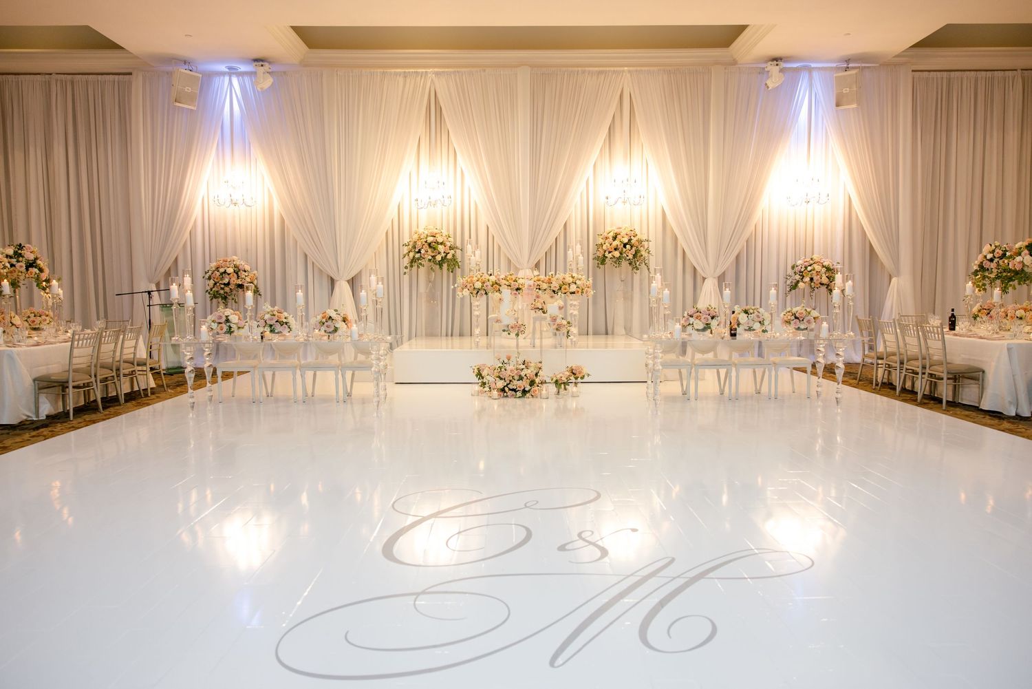 Opulent white ballroom with draped walls, crystal chandeliers and monogrammed dance floor.