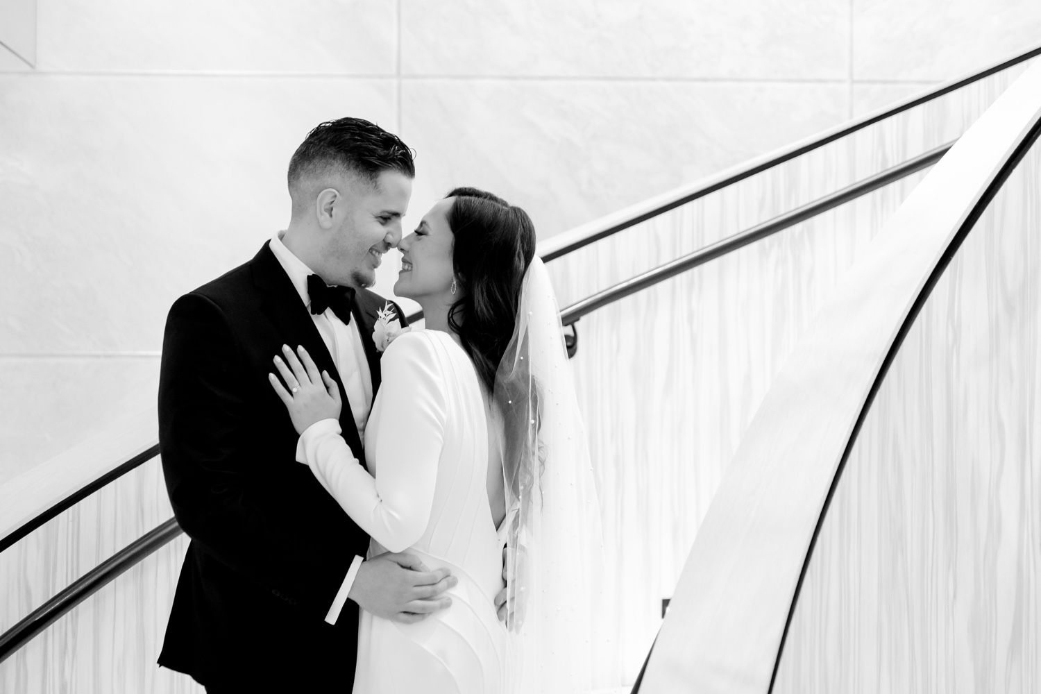 Intimate black and white portrait of newlyweds embracing against curved staircase backdrop.