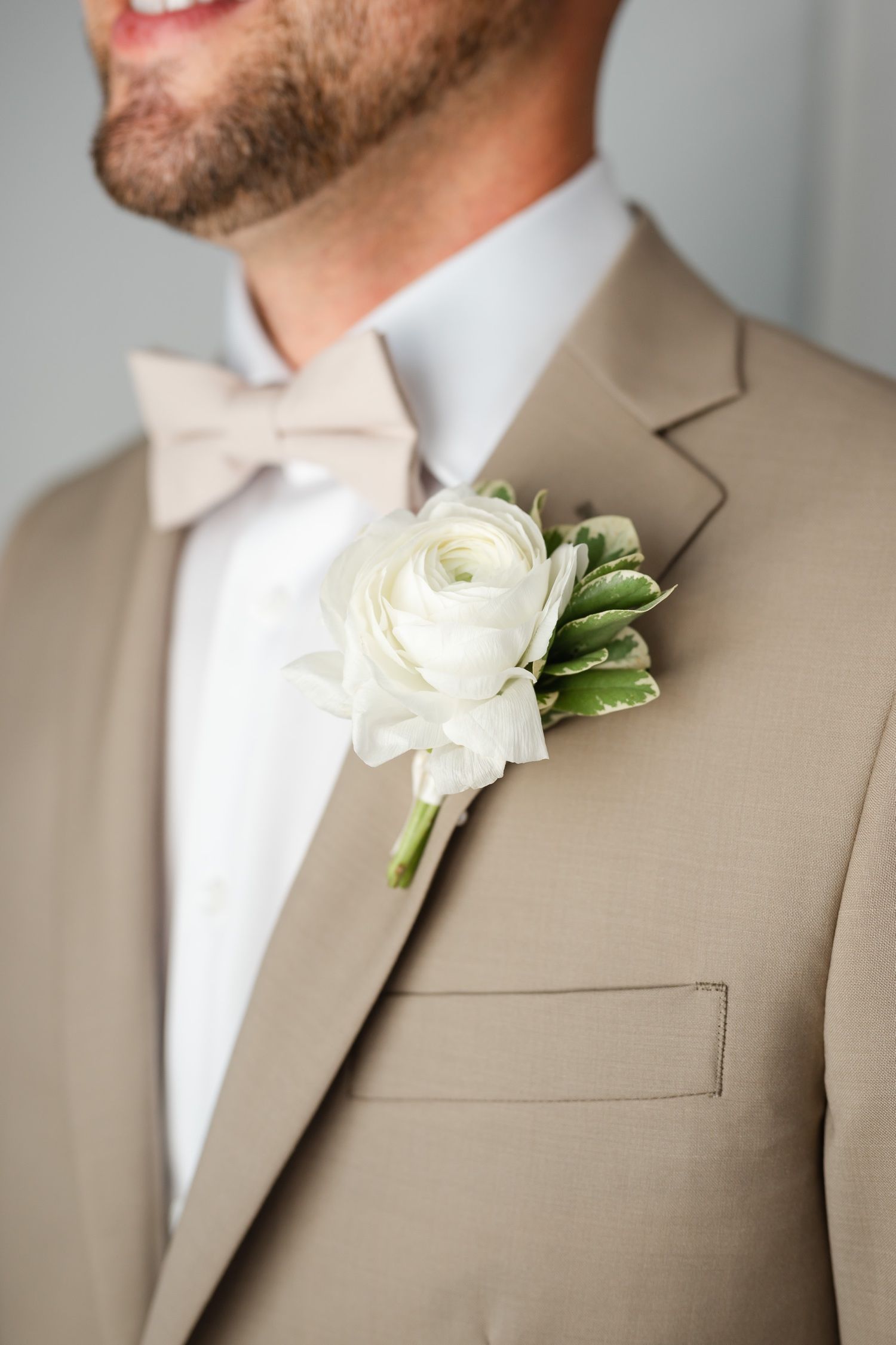 Close-up detail of a white ranunculus boutonniere on a beige suit lapel.