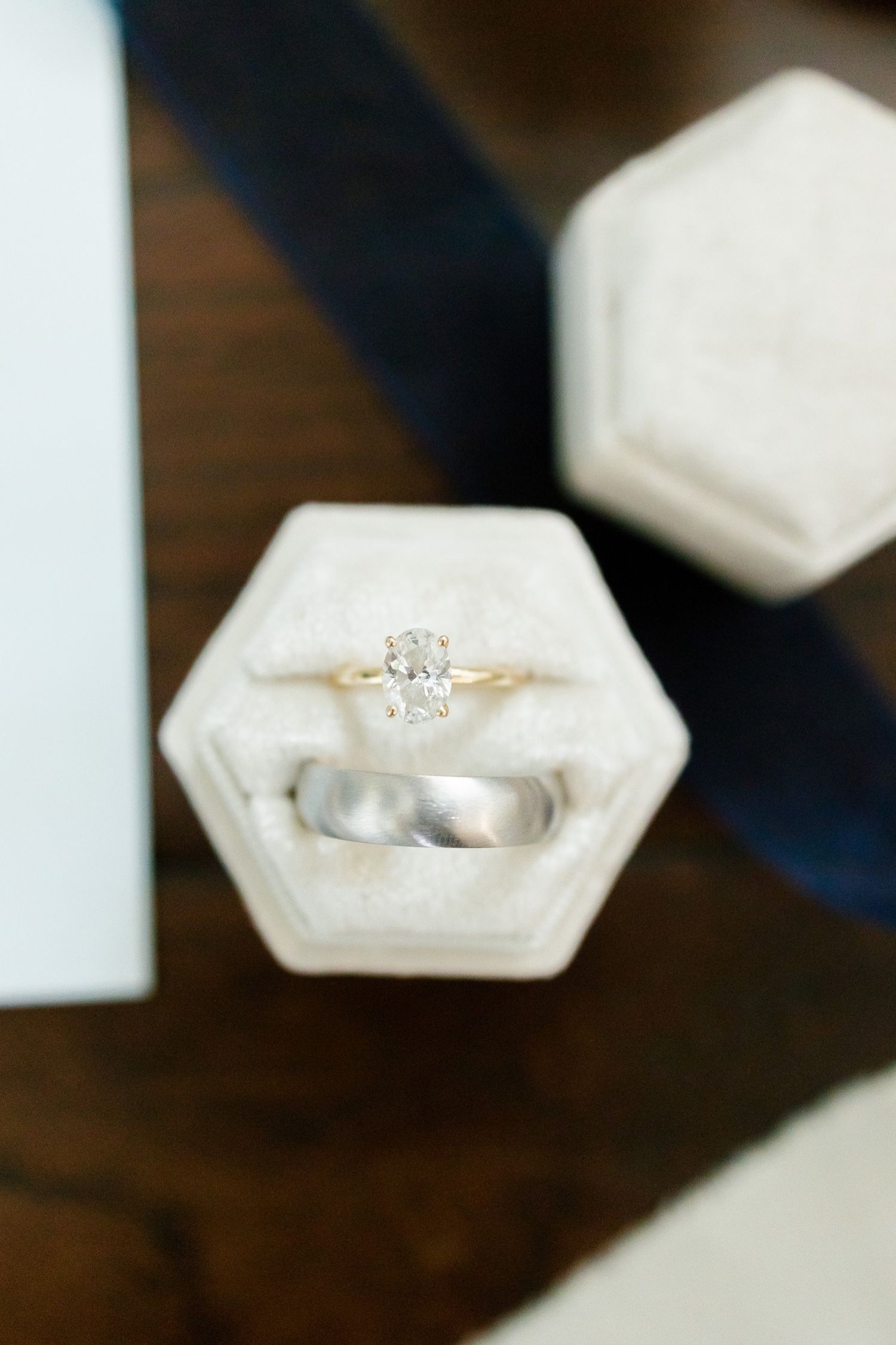 Wedding rings displayed in a white hexagonal holder featuring a solitaire diamond engagement ring and plain band.