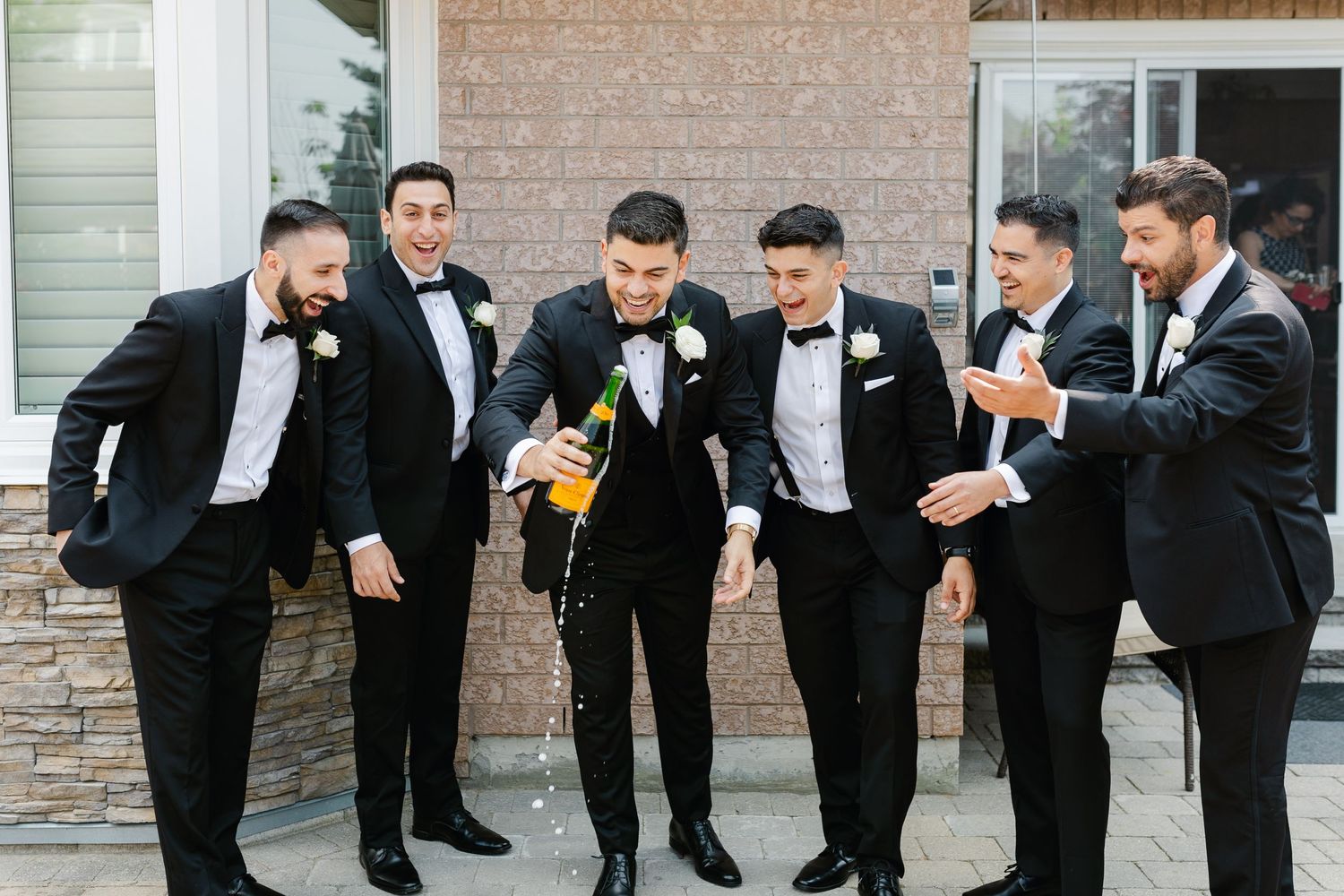 Wedding party having fun and laughing together while wearing matching black tuxedos.