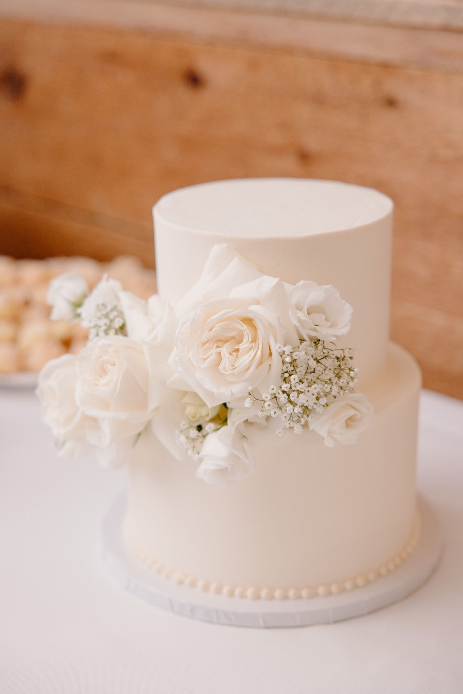Two-tier white wedding cake decorated with fresh white roses and baby's breath.