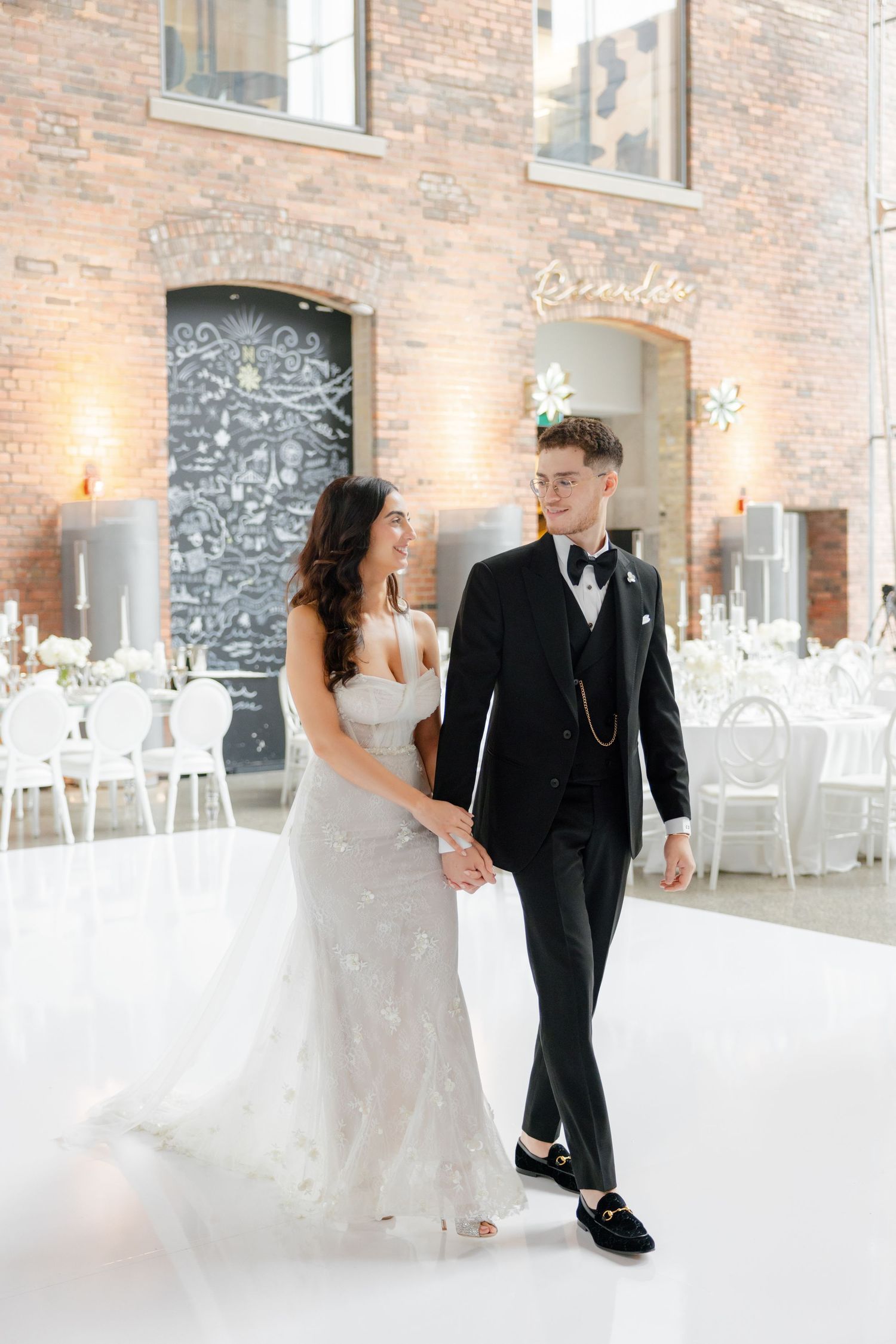 Couple walking hand in hand through their elegantly decorated reception venue.