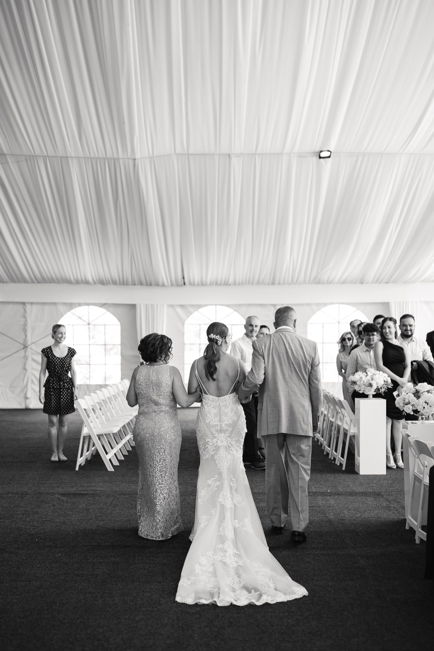 A black and white photo capturing an intimate wedding ceremony moment under an elegant draped tent.