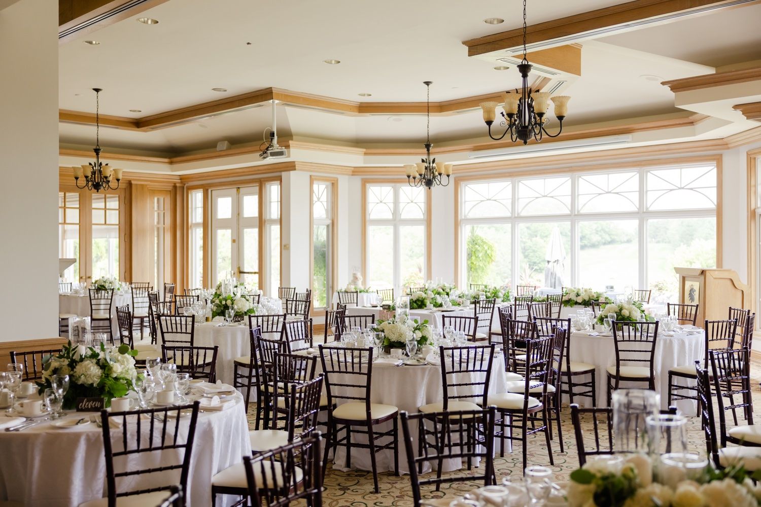 Elegant reception venue with Chiavari chairs and chandeliers set for wedding celebration.