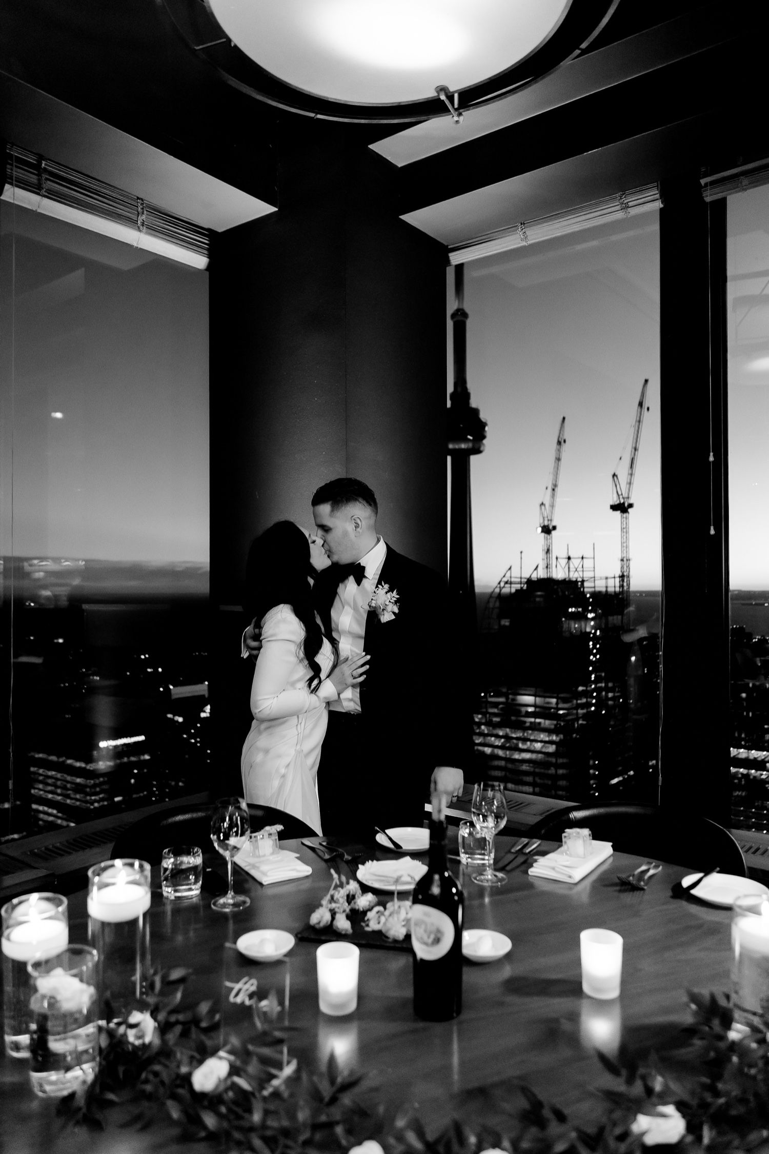 Romantic candlelit dinner at a high-rise restaurant with city views and construction cranes visible through windows.