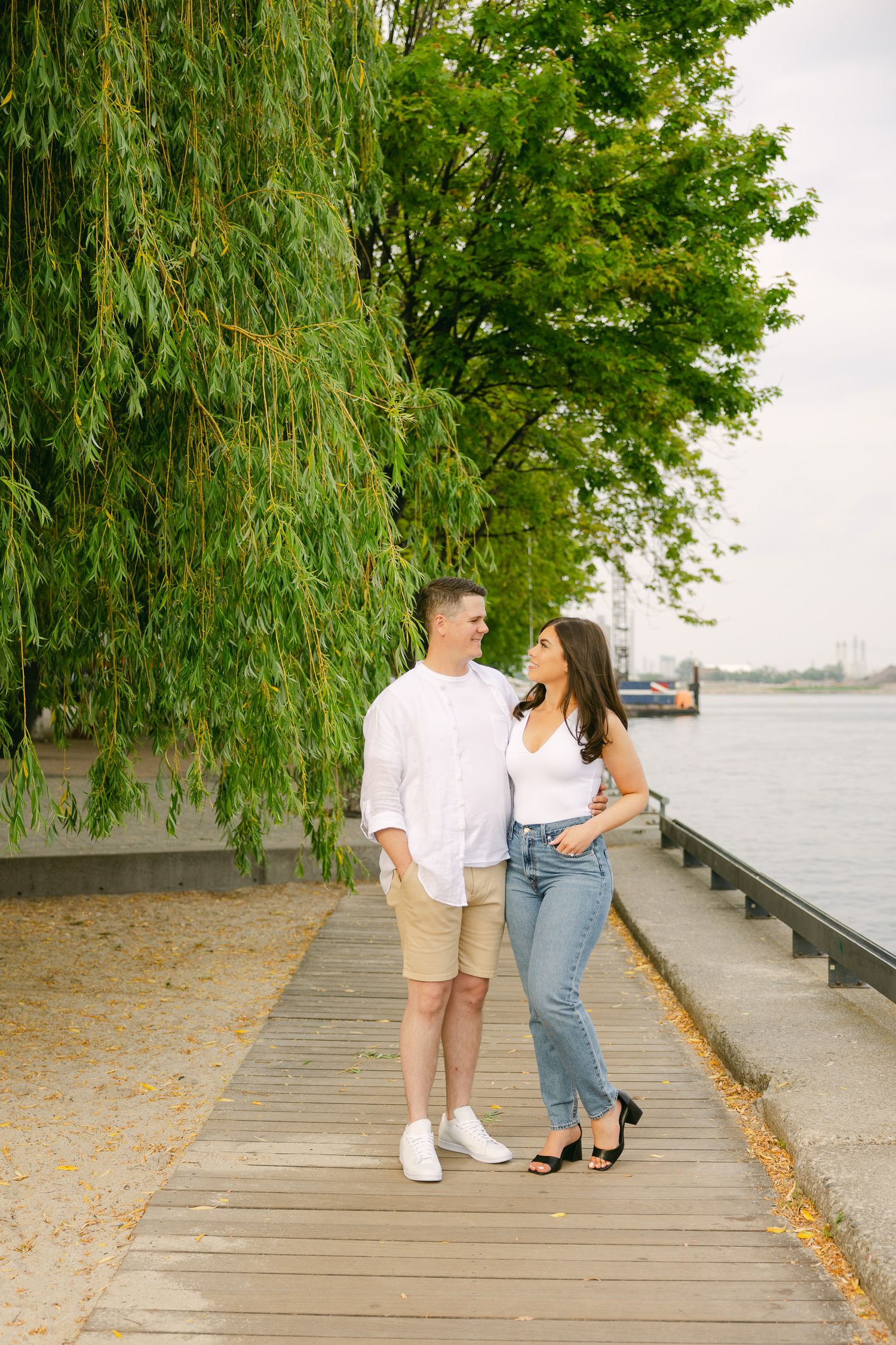 Couple in casual summer outfits sharing romantic moment on boardwalk by river.