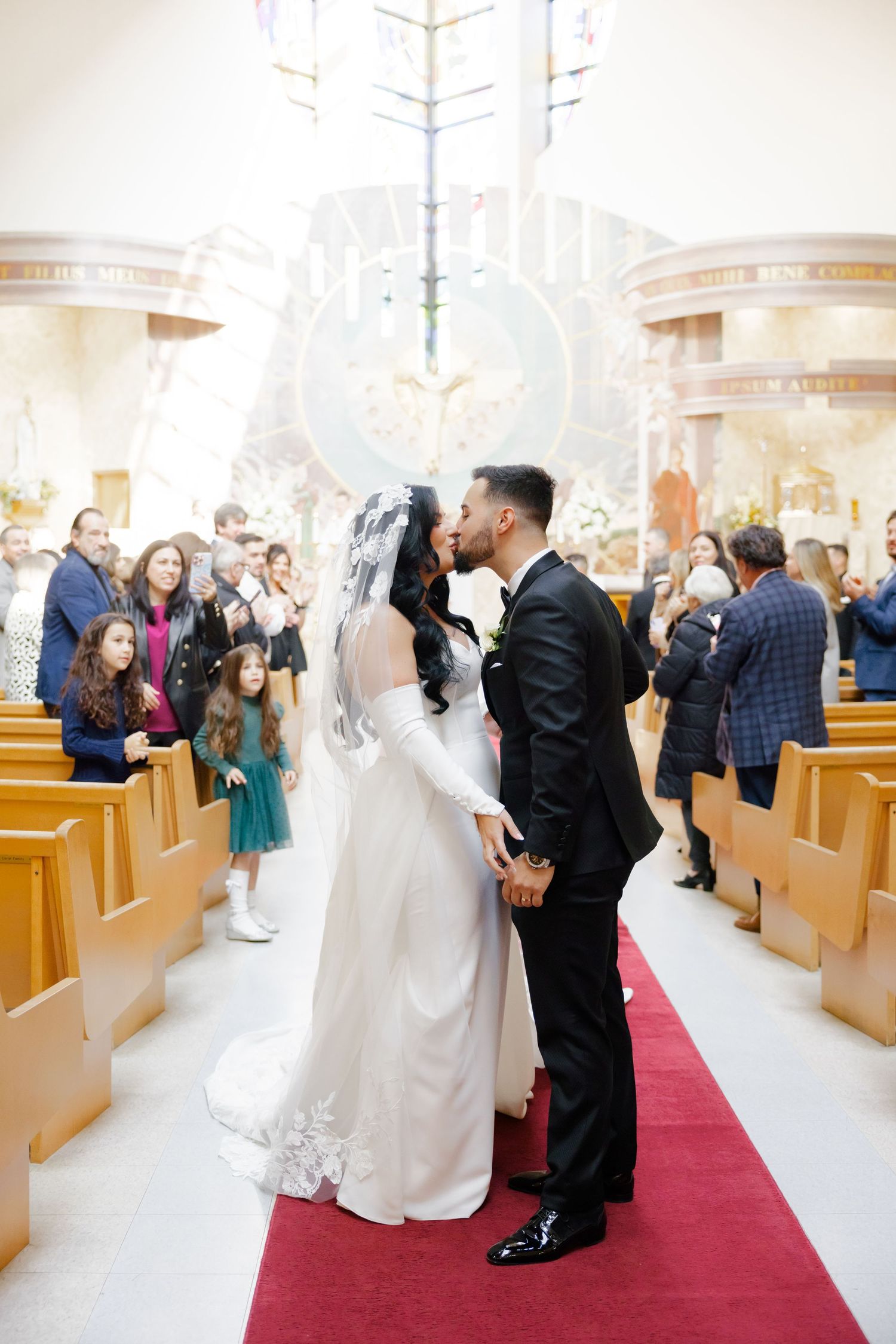 A wedding couple shares an intimate moment in the church aisle as guests look on.