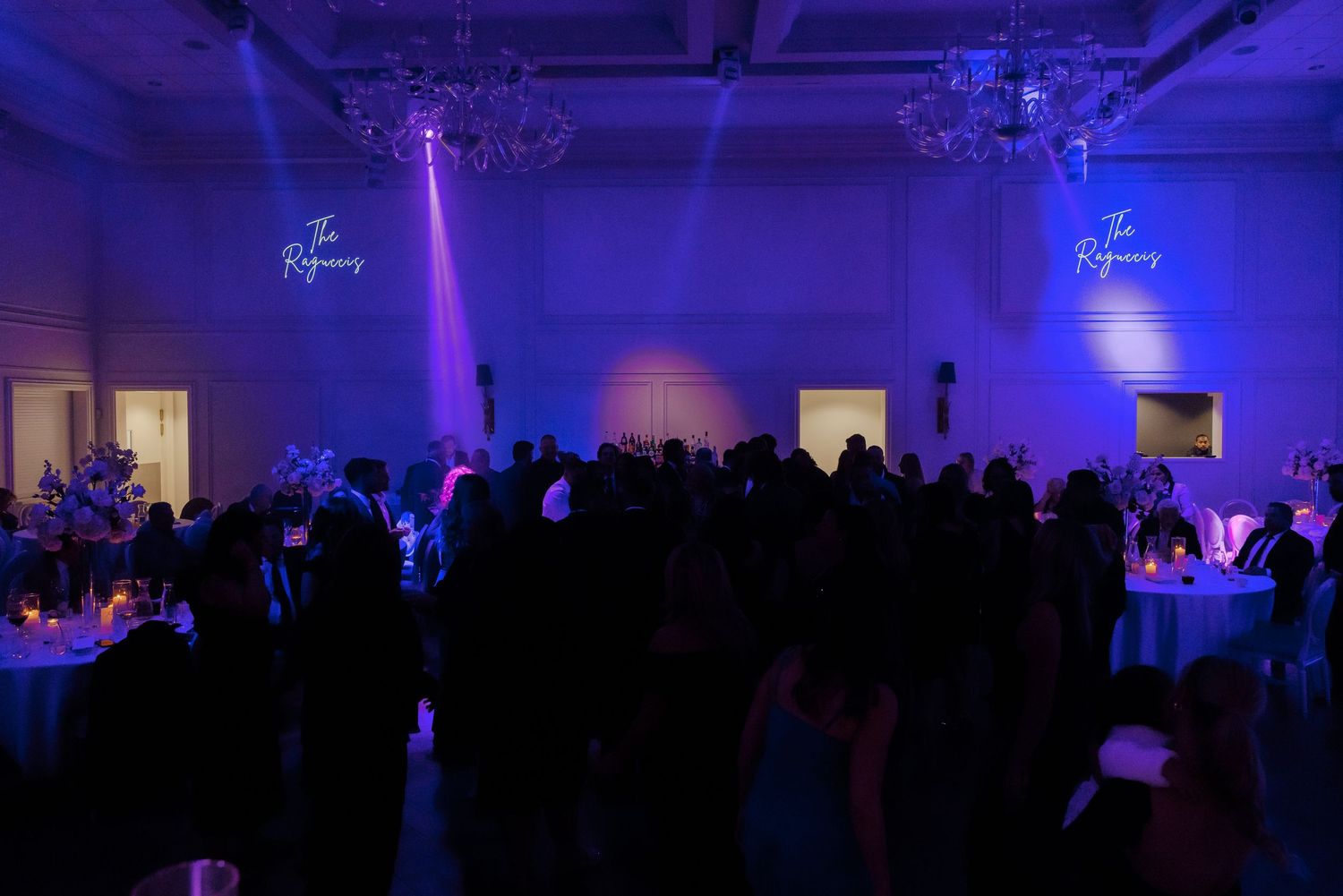 Dark reception hall illuminated with blue lighting and filled with wedding guests.