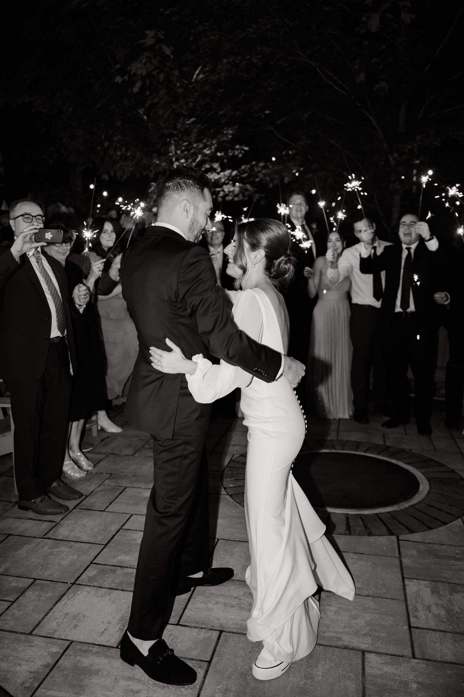 A couple shares their first dance surrounded by guests with sparklers at night.