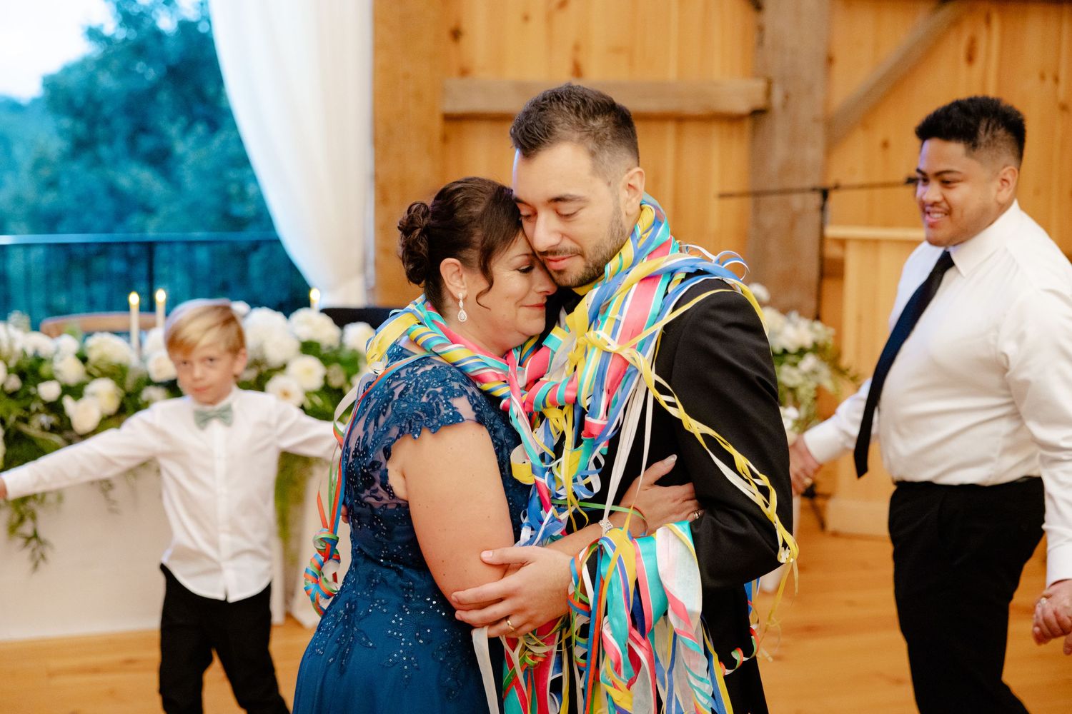 A heartwarming dance moment with festive streamers at a rustic barn wedding venue.