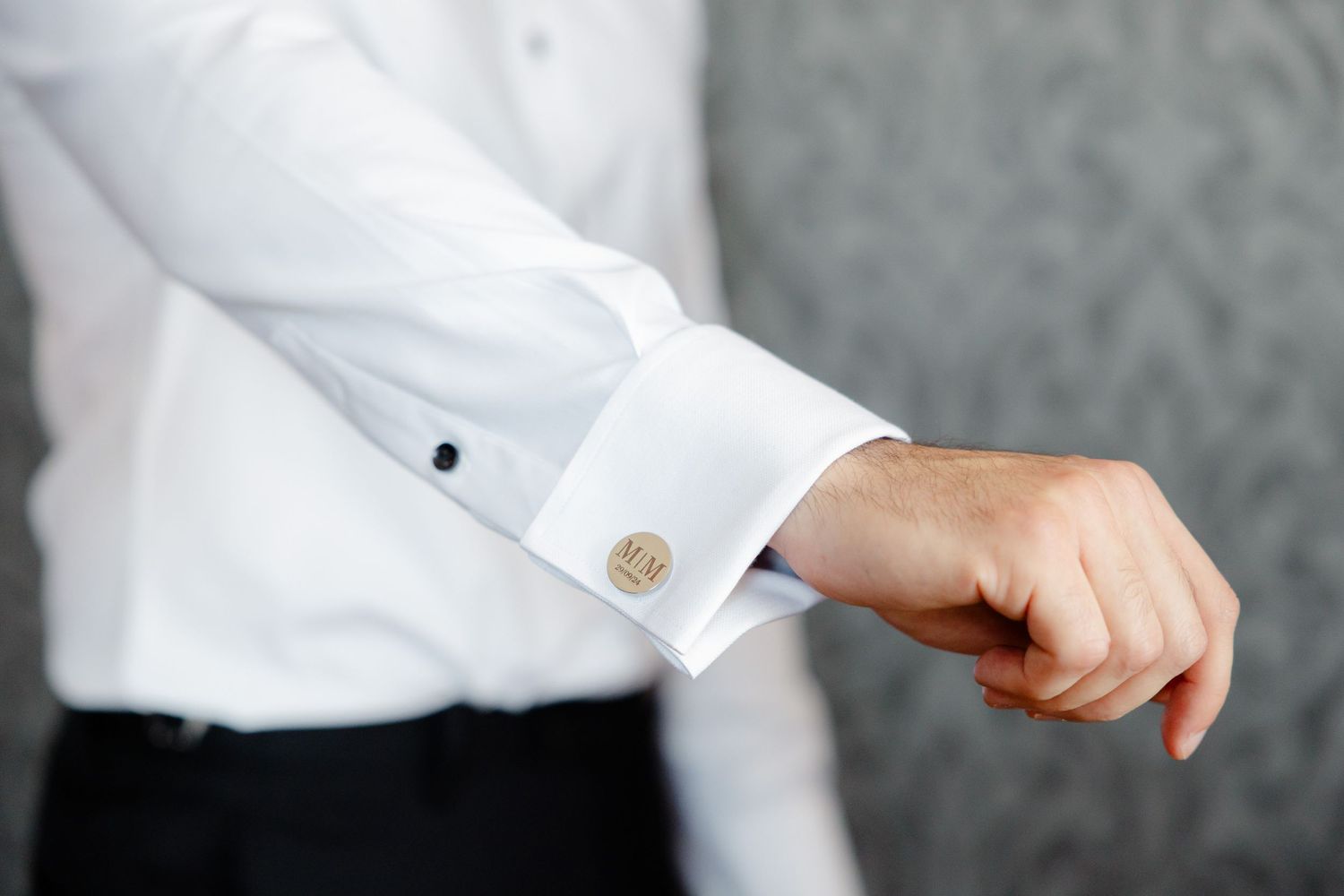 Close-up of gold cufflink on white dress shirt sleeve during wedding preparations.