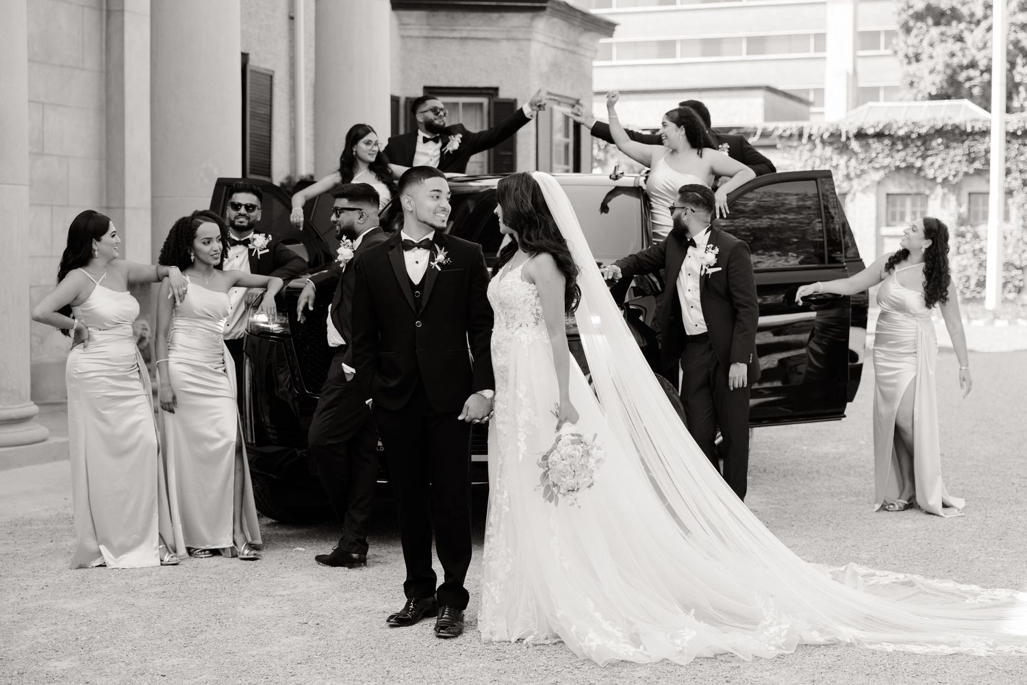Black and white photo of wedding party celebrating outside historic building with columns.