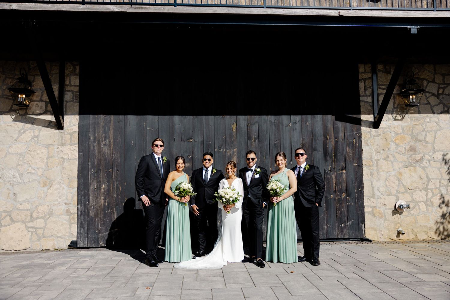 A wedding party poses formally in front of a dark wooden barn door with bridesmaids in mint green dresses.