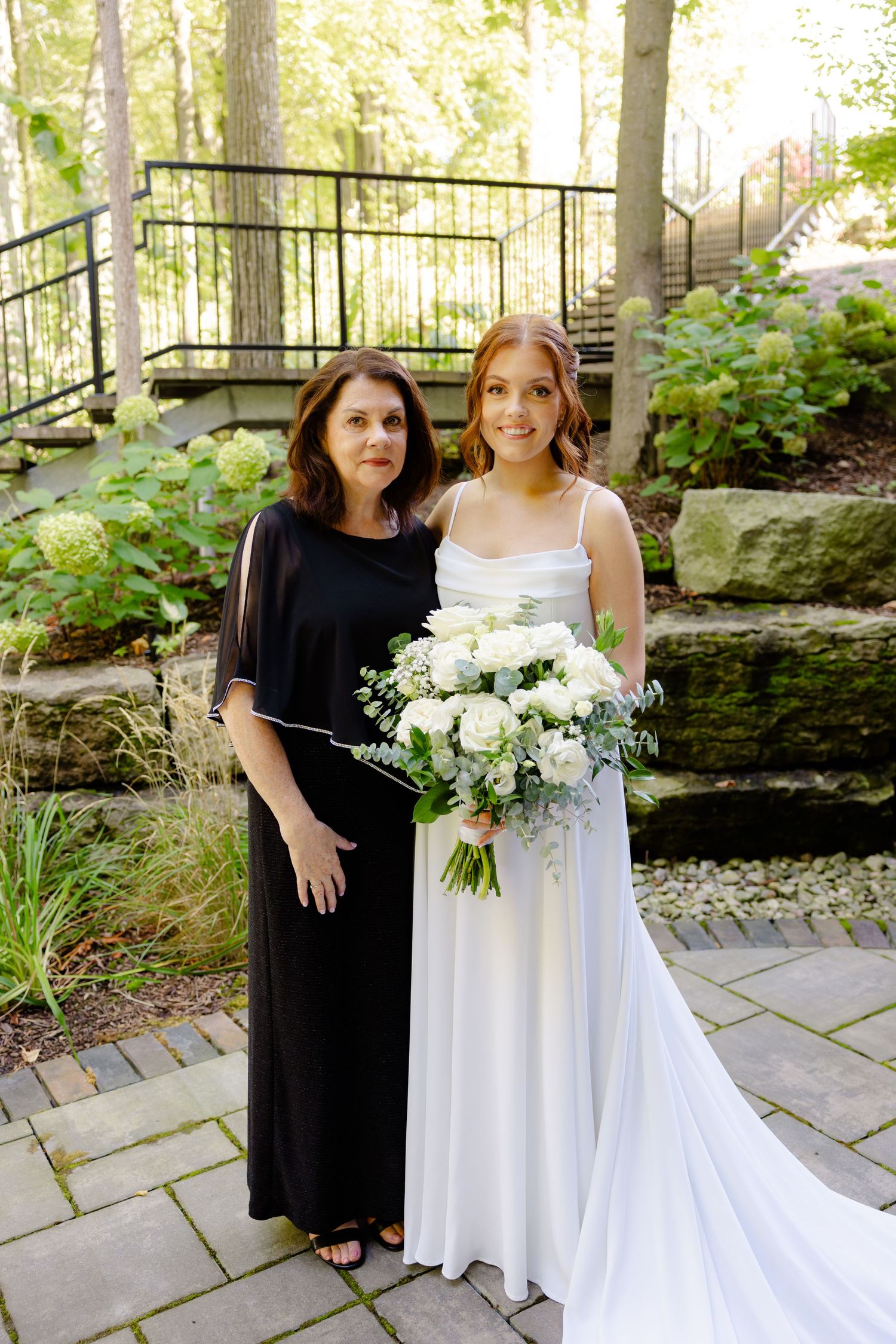A formal portrait in a garden setting with a beautiful white bridal bouquet.