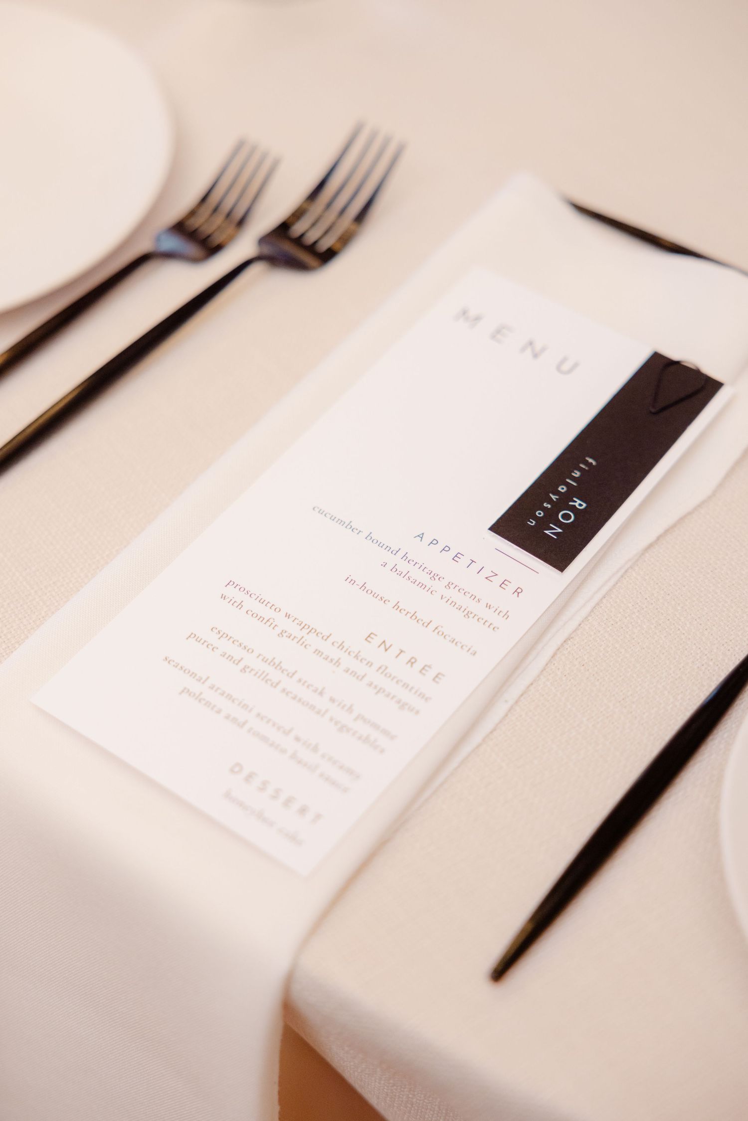 Minimalist wedding menu card with black accent placed on white tablecloth with silverware.
