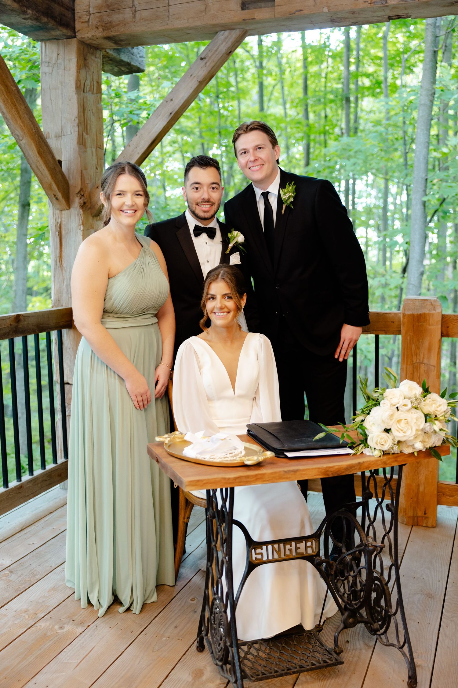 Wedding party gathered around vintage Singer sewing table during forest pavilion ceremony.