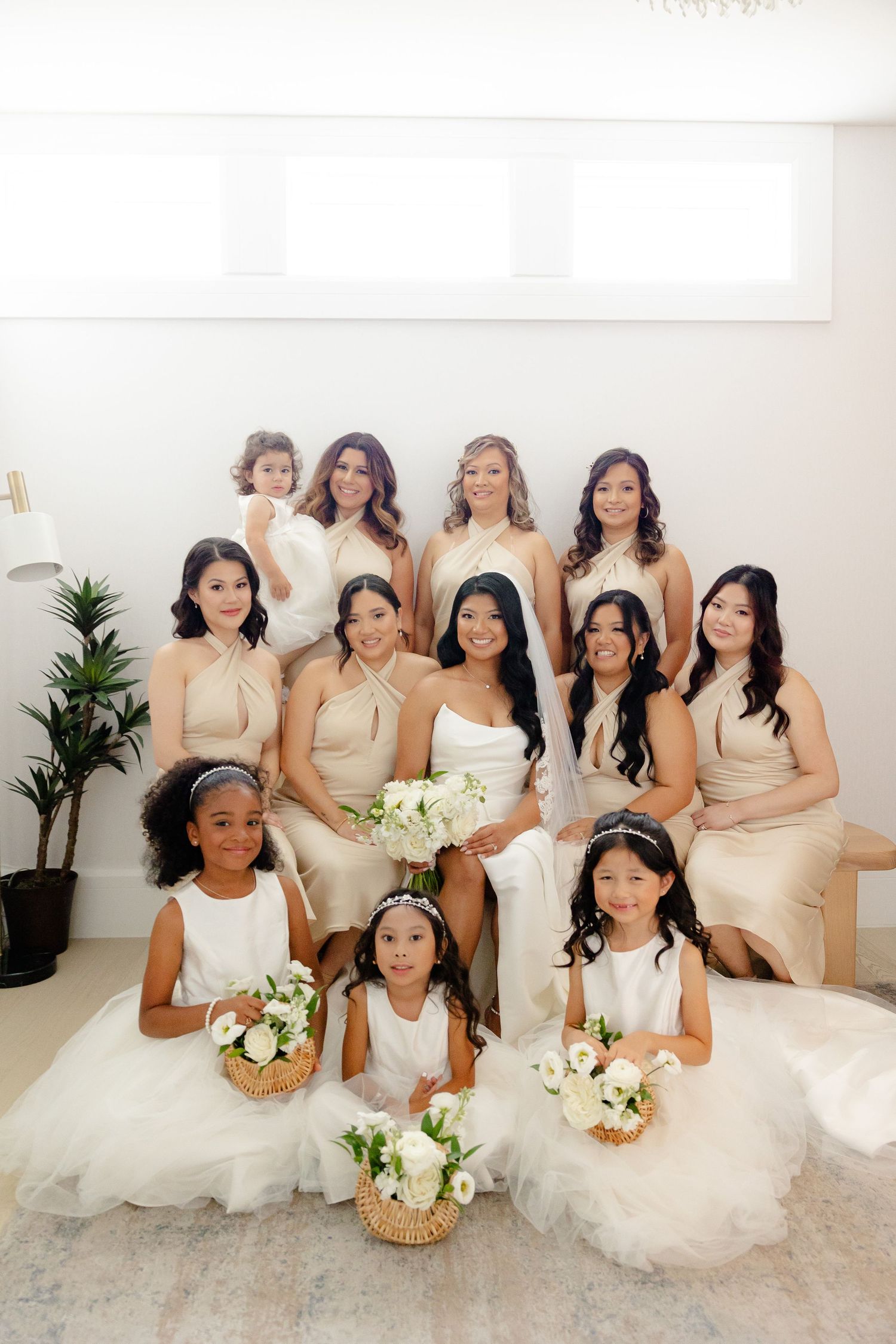 Formal group portrait of bridesmaids and flower girls in cream dresses with white floral bouquets.