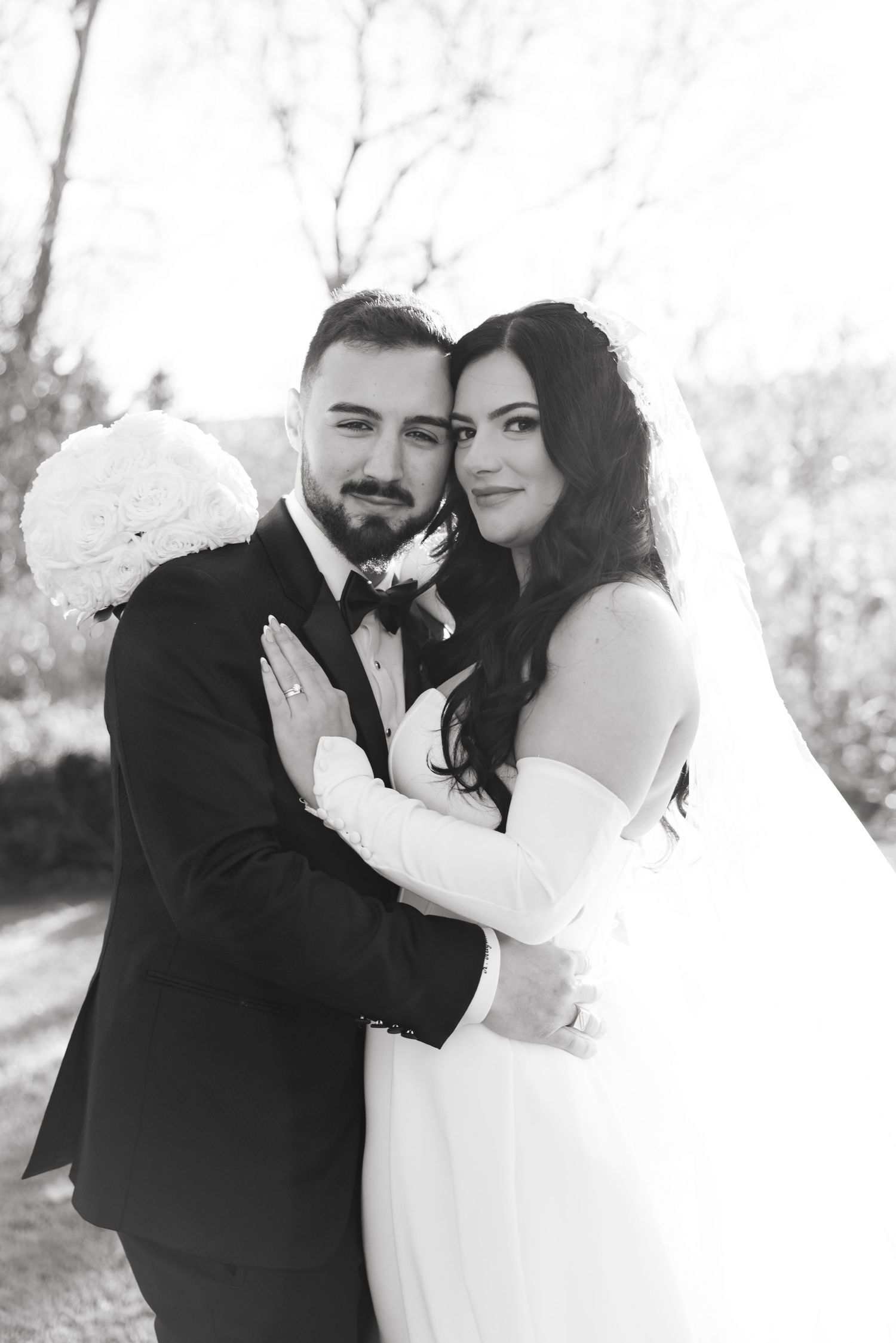 Black and white portrait of newlyweds embracing with bride holding white floral bouquet.