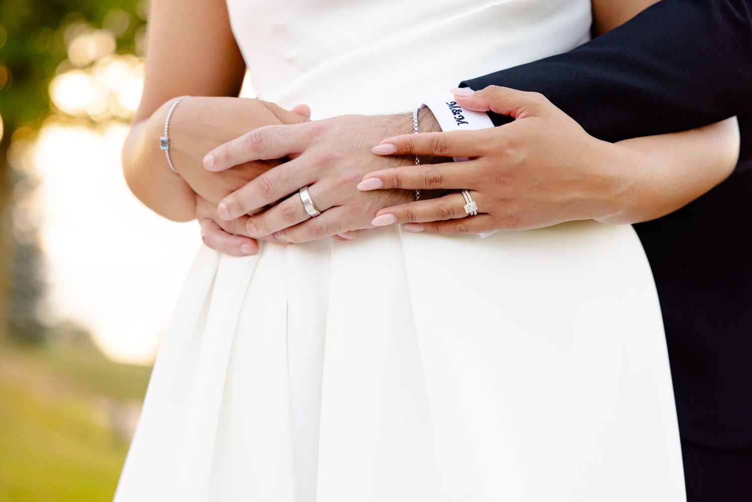Close-up of couple's hands with wedding rings against white bridal gown.