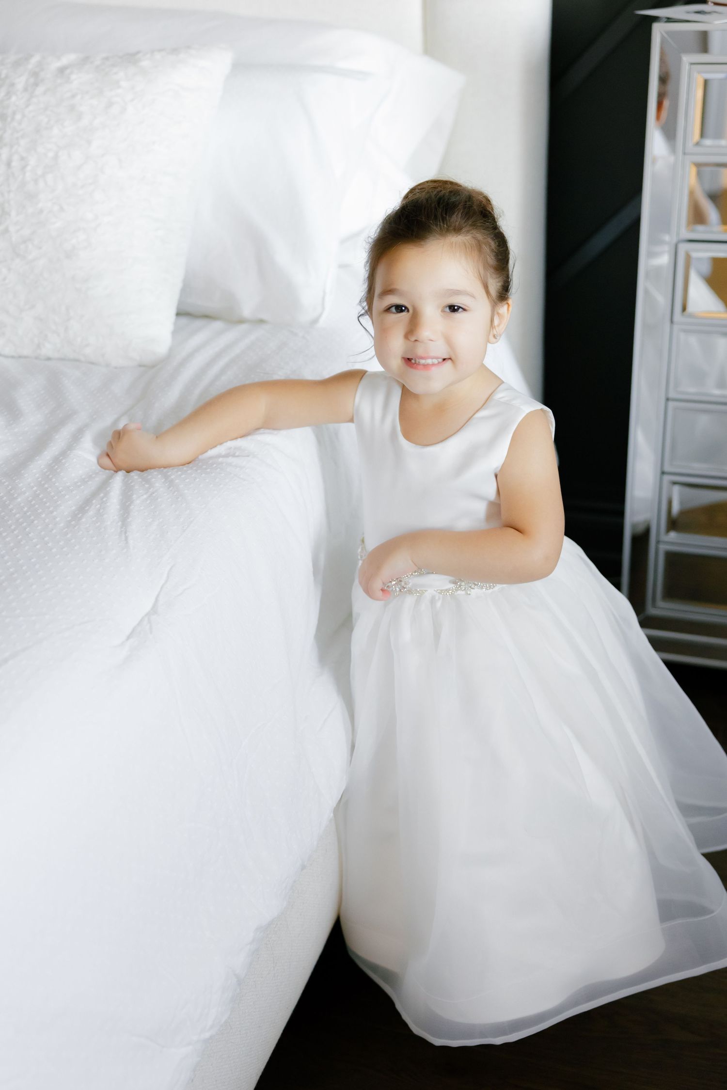 A young child in a white dress smiles while holding onto fluffy white fabric.