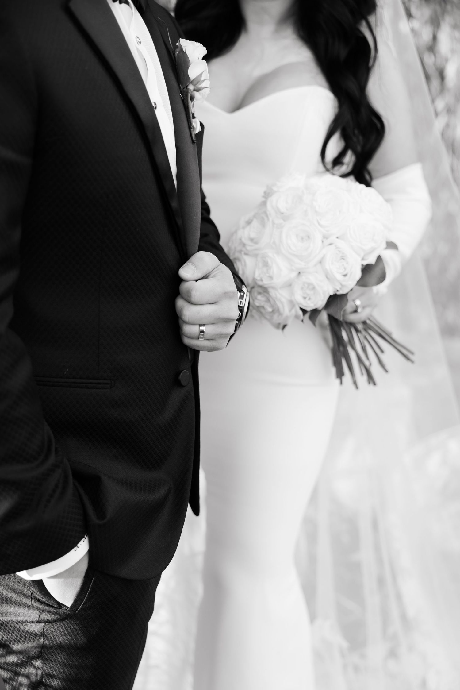 Black and white close-up of wedding couple holding bouquet of white roses.