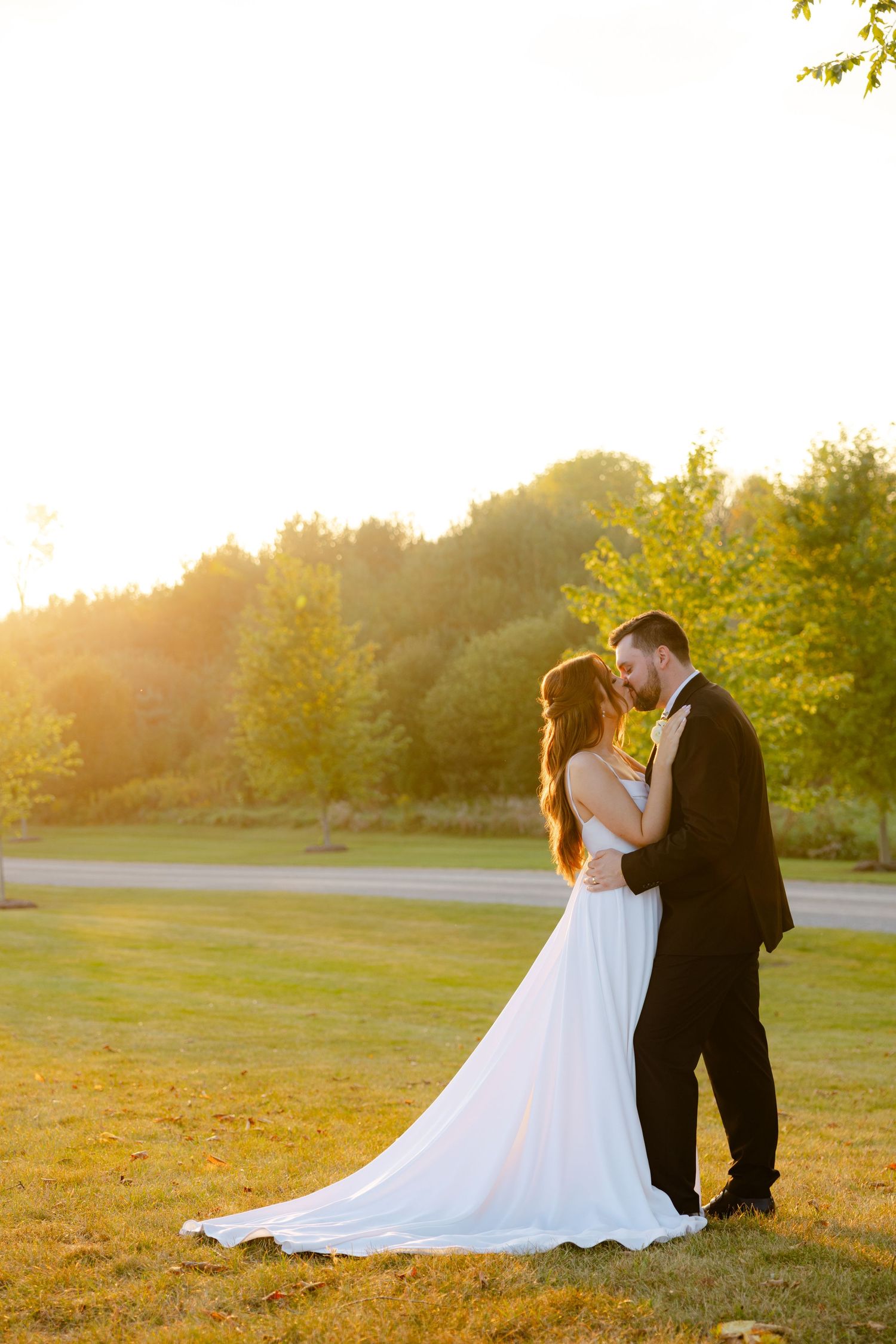 Wedding couple stands close together against a backdrop of sunlit trees during their outdoor photoshoot.