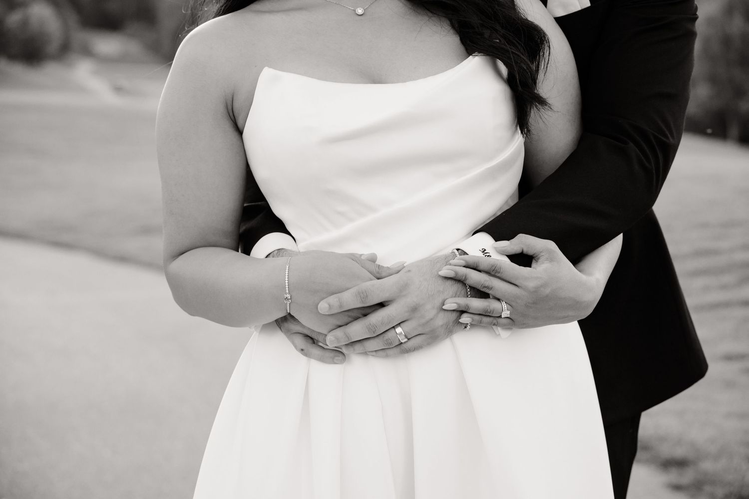 Close-up black and white photo of couple's hands embracing during wedding moment.