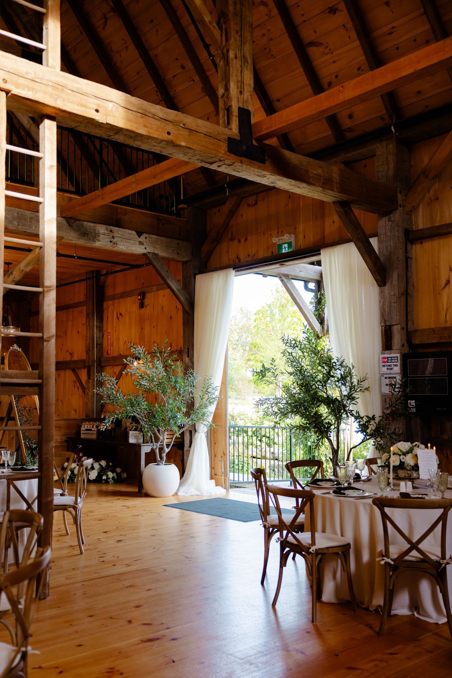 Rustic barn venue interior with wooden beams, natural light, and elegant table settings for a wedding reception.