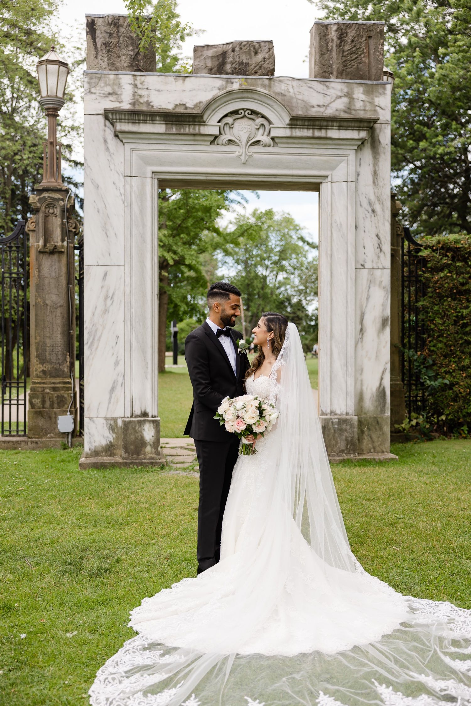 Romantic wedding portrait under ornate stone archway with dramatic cathedral length veil.