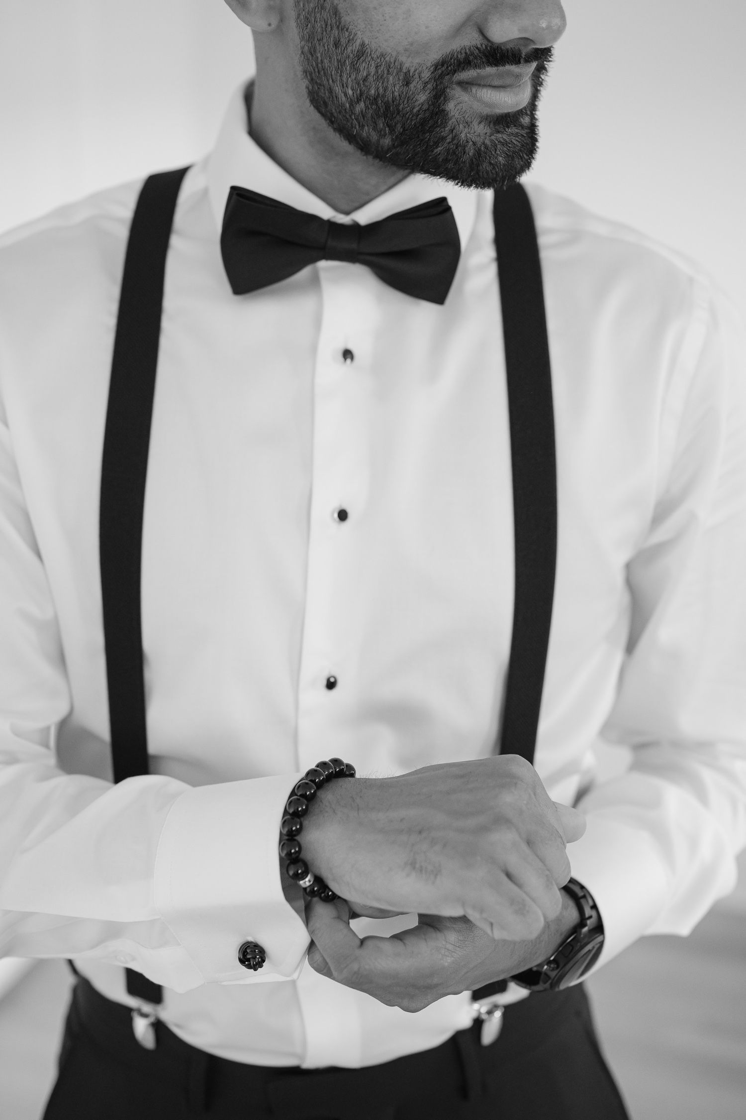 Close-up of formal attire showing black suspenders and bow tie against white shirt.