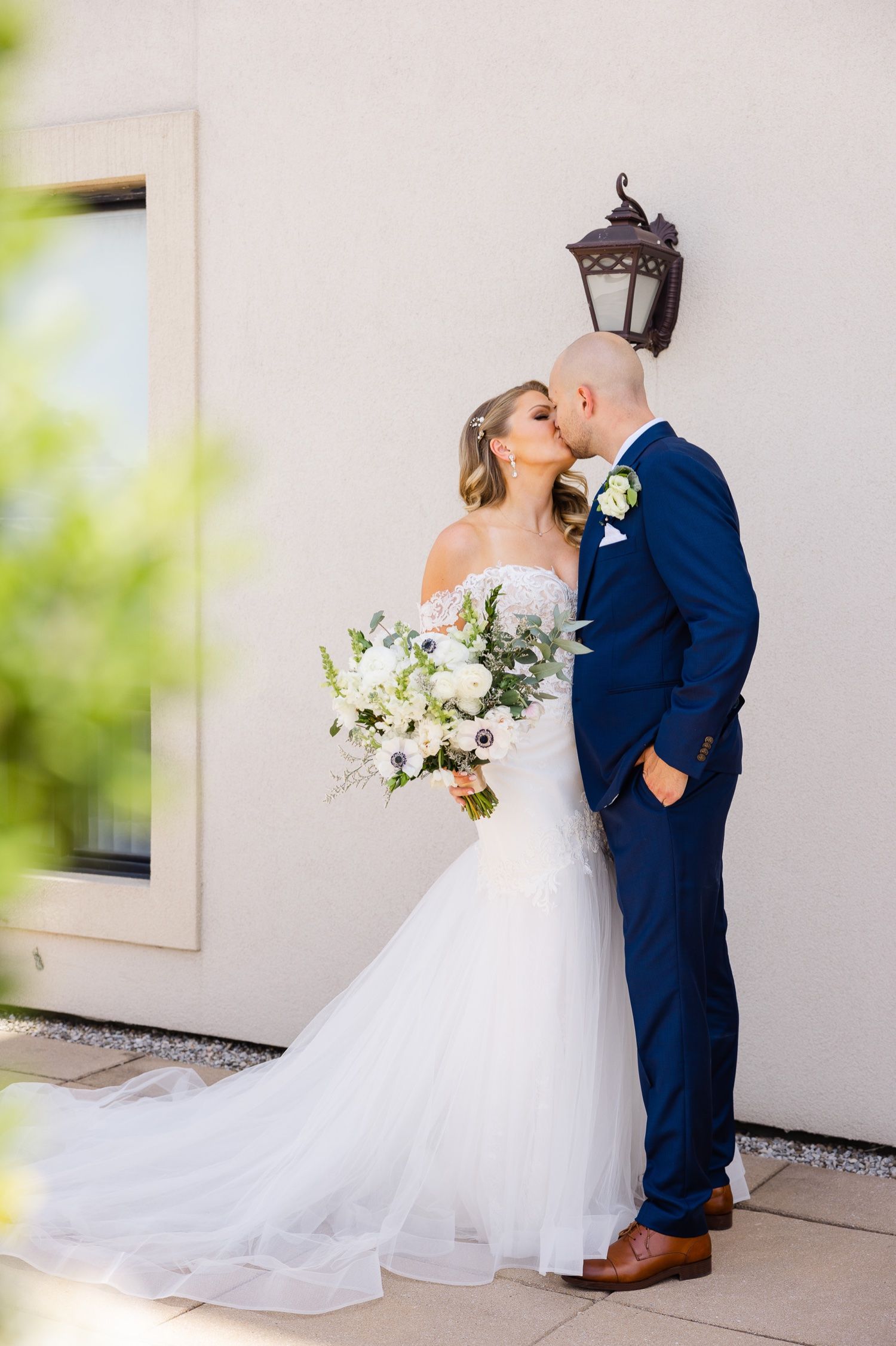Romantic wedding portrait against cream wall with vintage lantern and flowing white bridal bouquet.