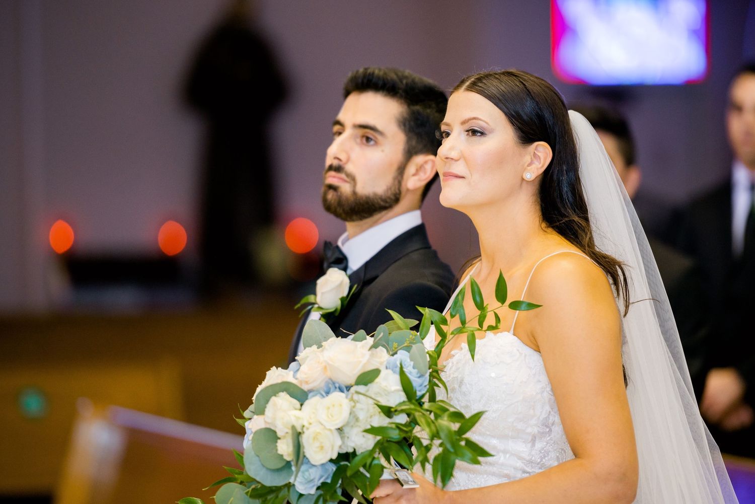 Close-up view of wedding couple at altar with white floral bouquet.