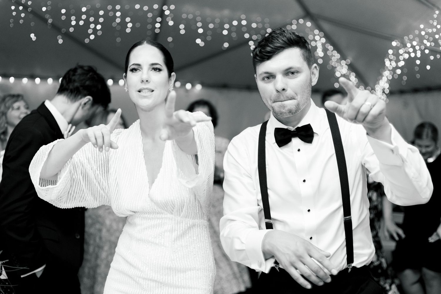 Wedding couple dancing joyfully under string lights at their reception.