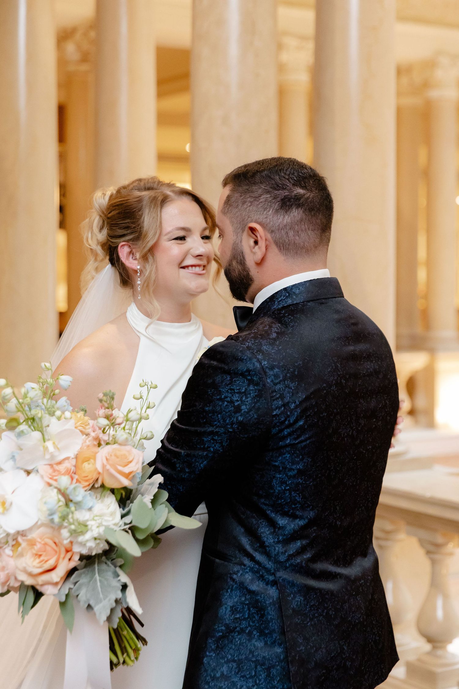 Romantic wedding couple shares intimate moments in an elegant hallway with classical columns.