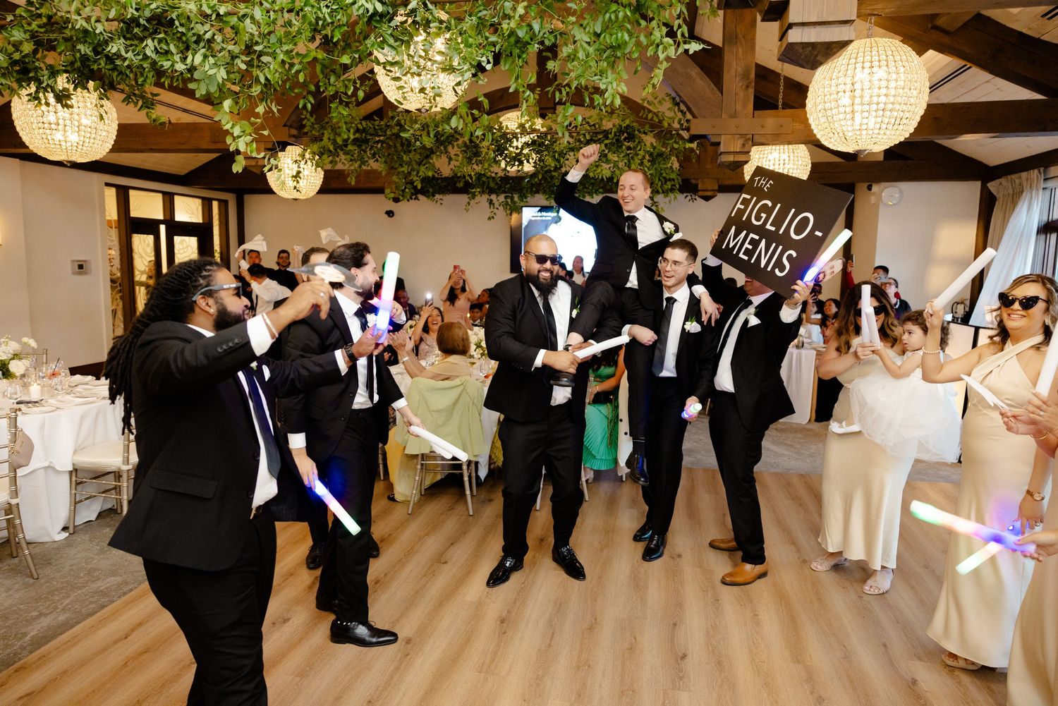 Wedding guests dance and celebrate on the dance floor under hanging lanterns and greenery.
