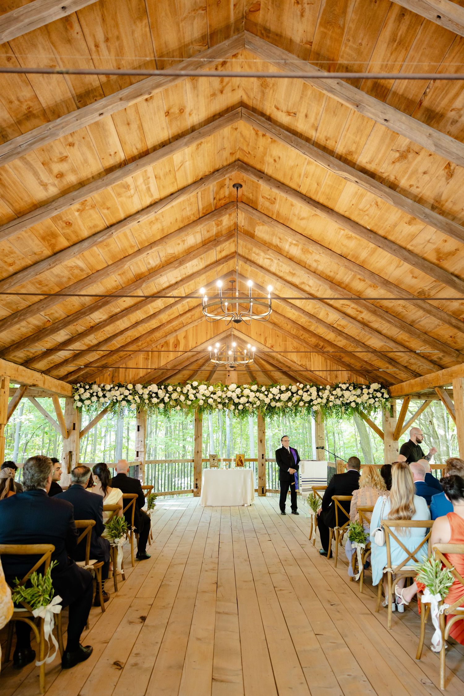 Wedding ceremony in a rustic wooden pavilion decorated with floral arrangements and chandeliers.