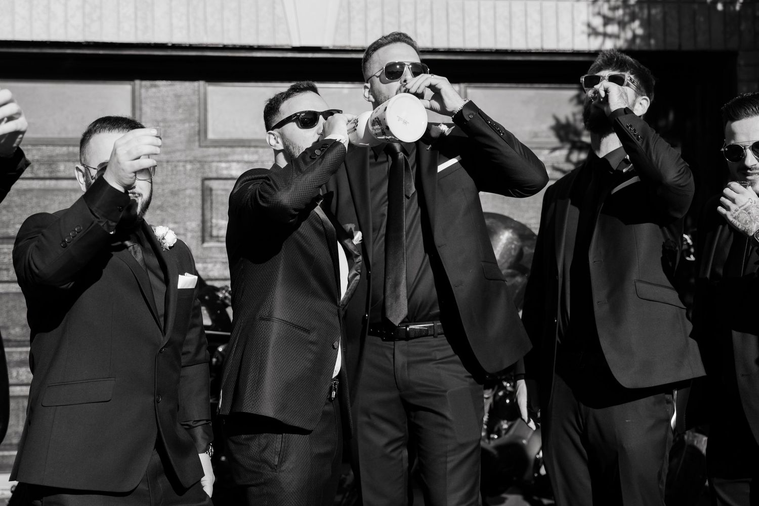 Wedding party in black suits takes a celebratory drink together in black and white photography.