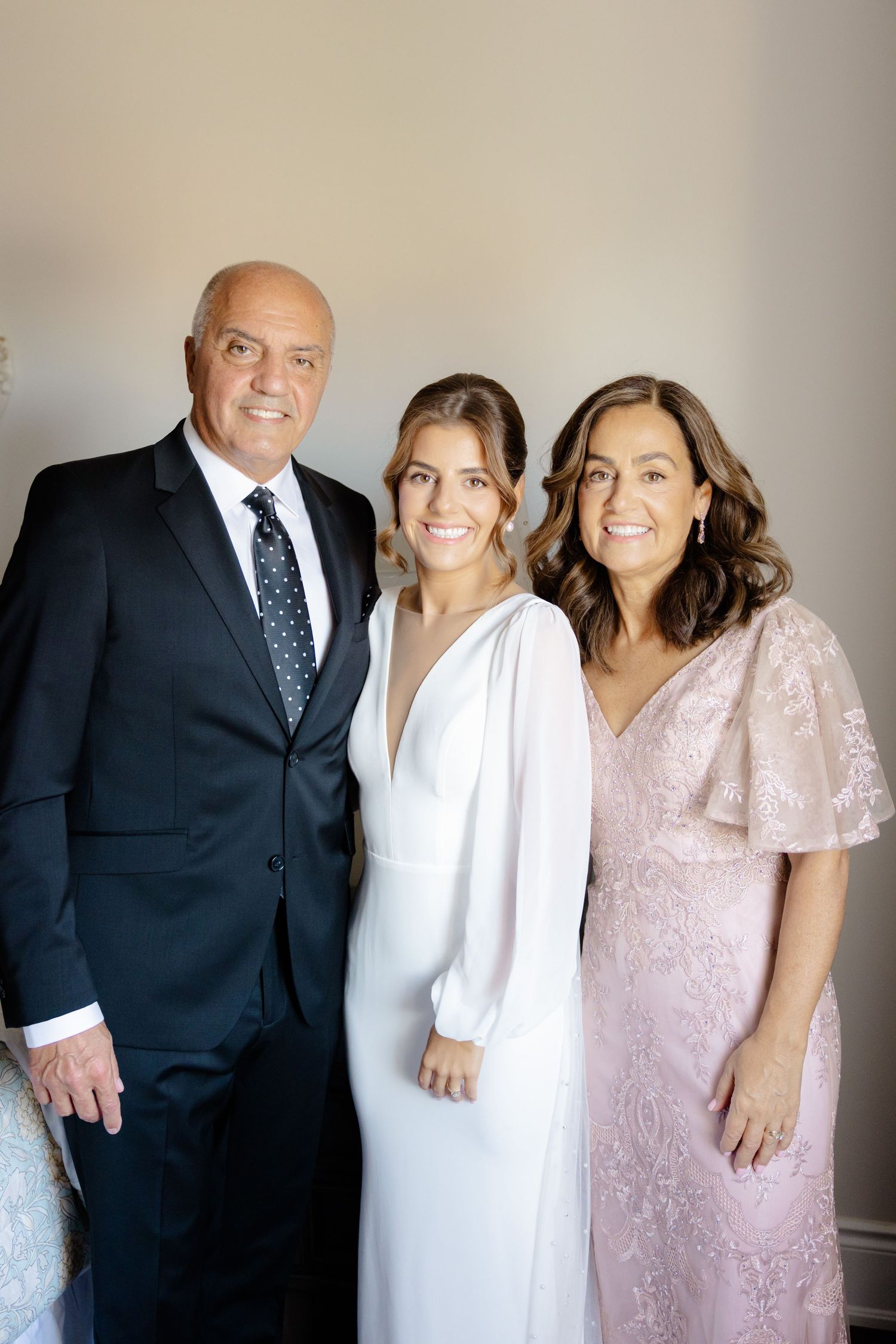 Wedding party portrait featuring bride in white dress with two family members in formal attire.