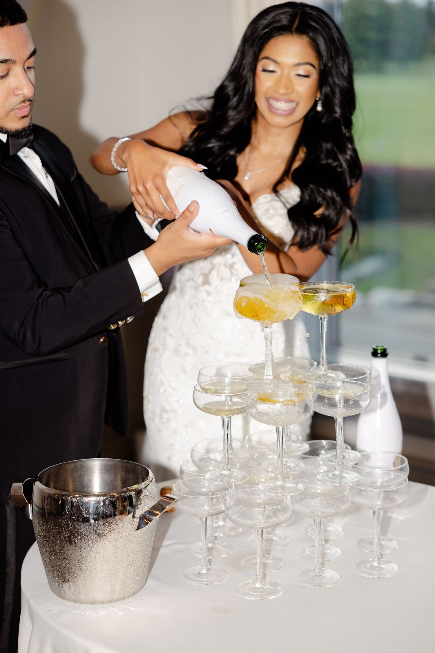 A couple joyfully builds a champagne tower together during their wedding celebration.
