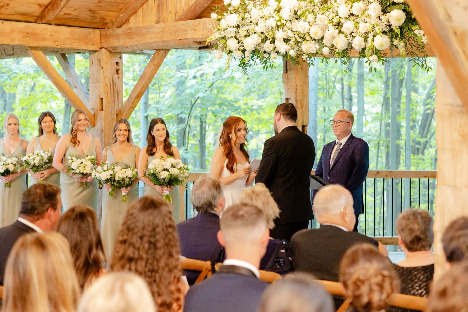 Intimate forest wedding ceremony with guests seated in wooden chairs under vaulted timber ceiling.