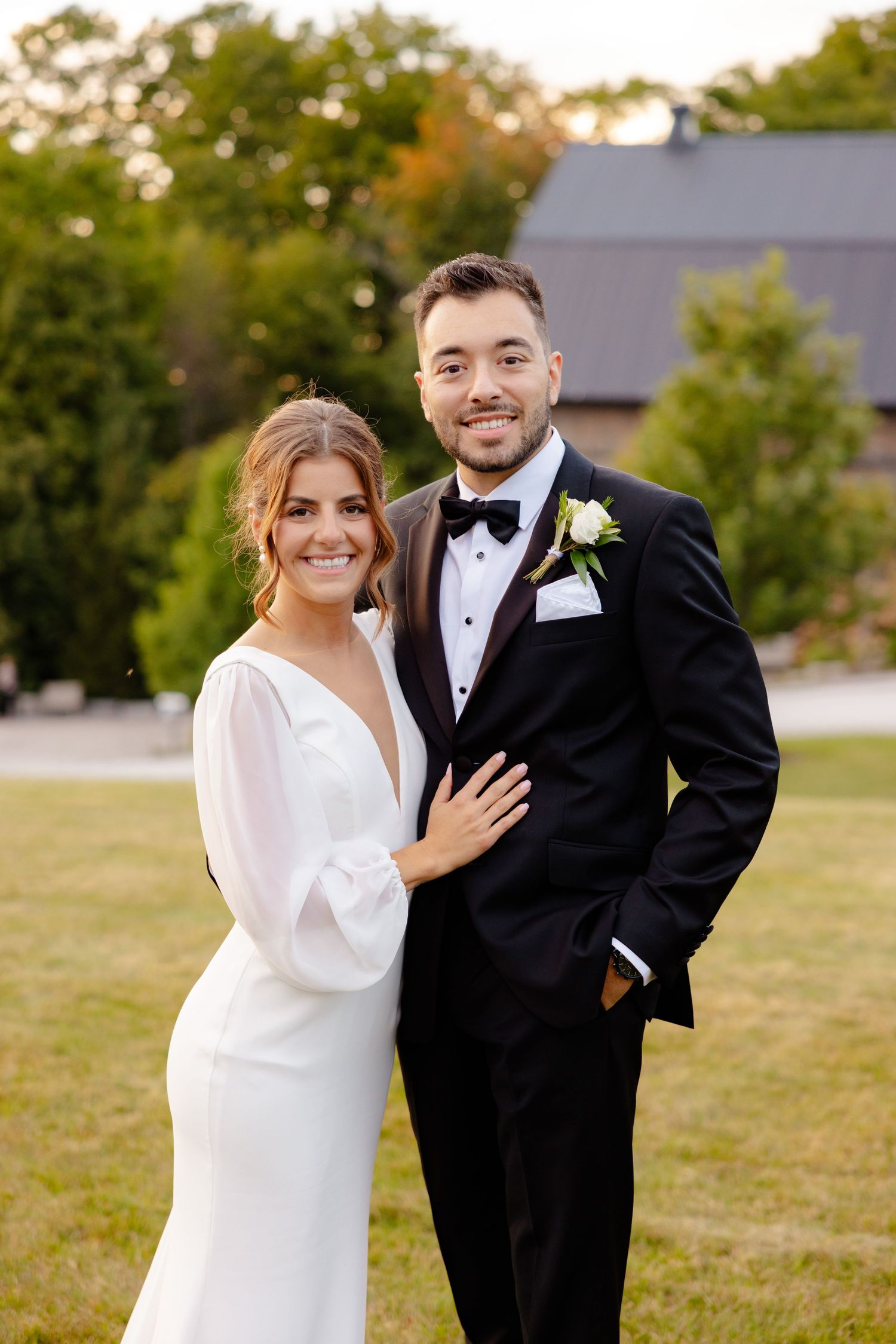A wedding portrait featuring a couple in classic black and white attire against a rustic backdrop.