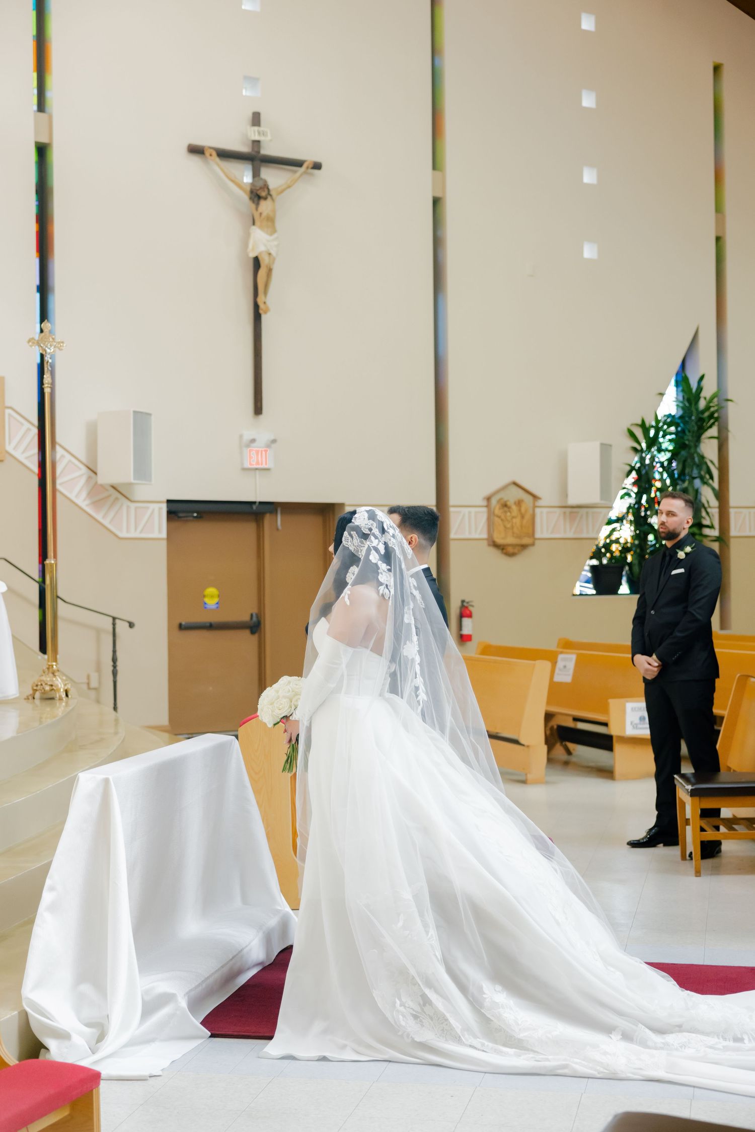 A wedding dress with long train in front of a church crucifix.