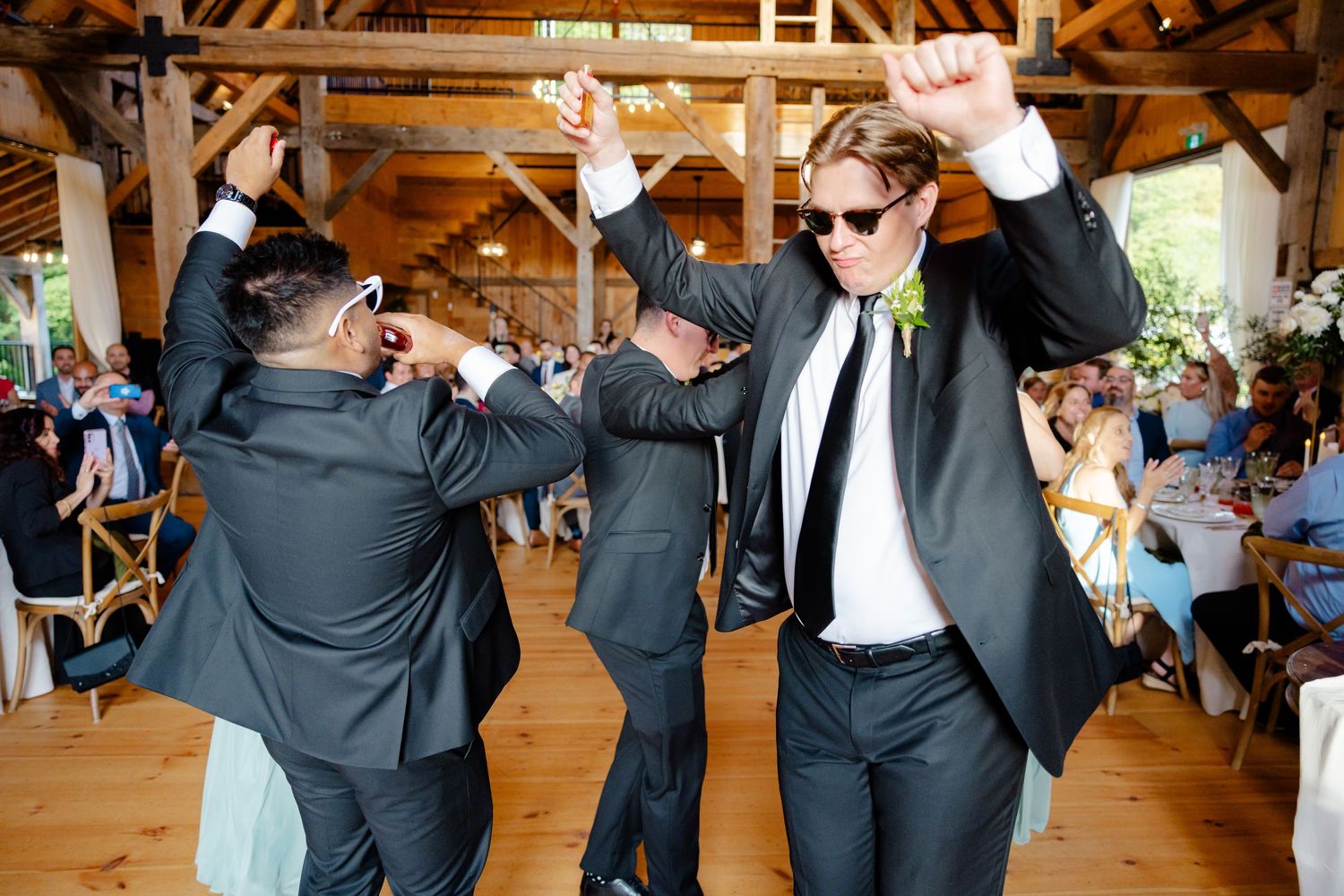 Celebratory dancing scene in a rustic barn wedding venue with formal attire.