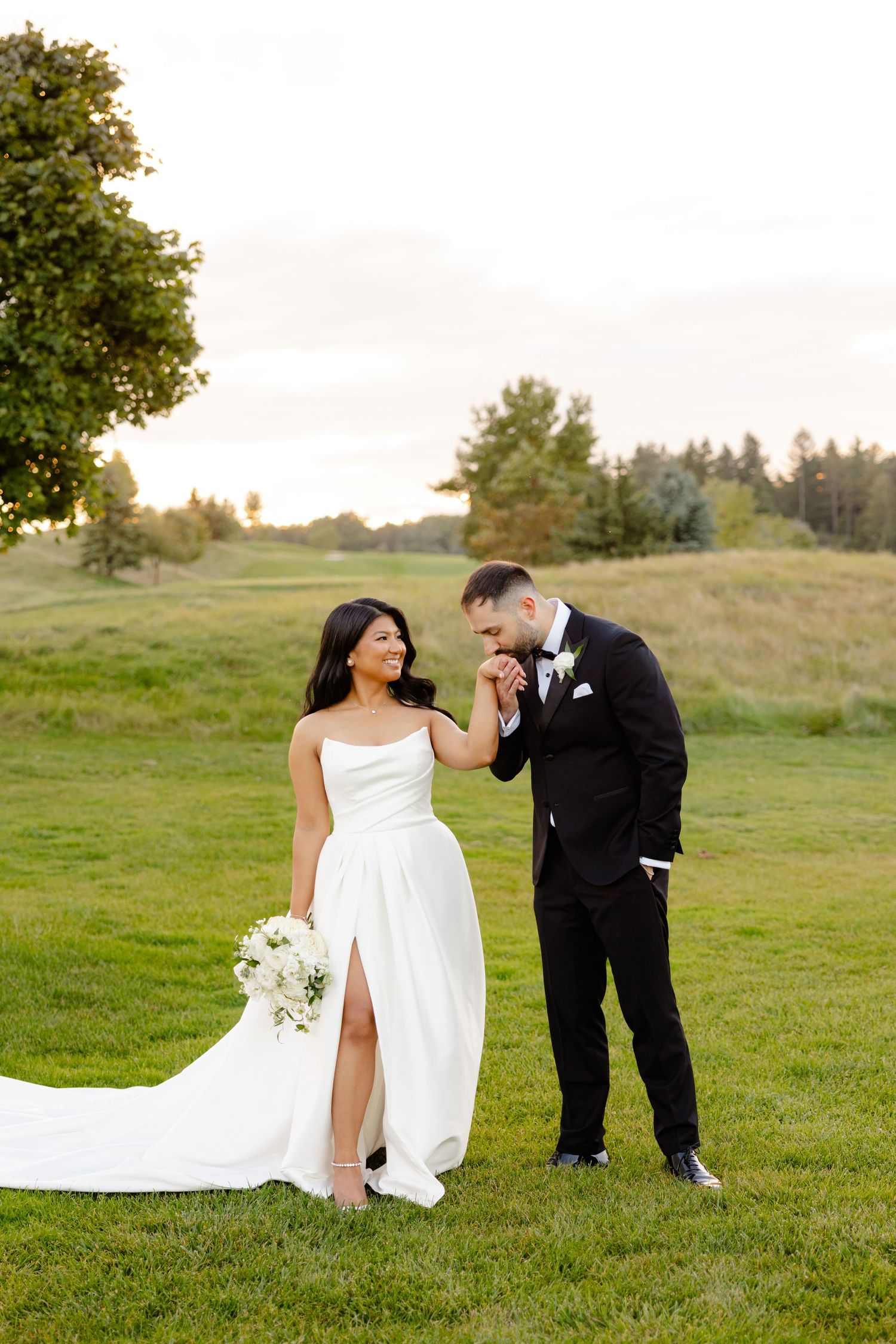 A romantic wedding moment captured on a grassy hill with a beautiful tree in the background.